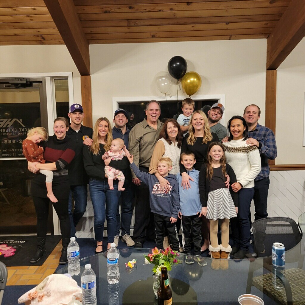 Large group of family and friends posing together indoors for a photo, some holding children, with balloons in the background.