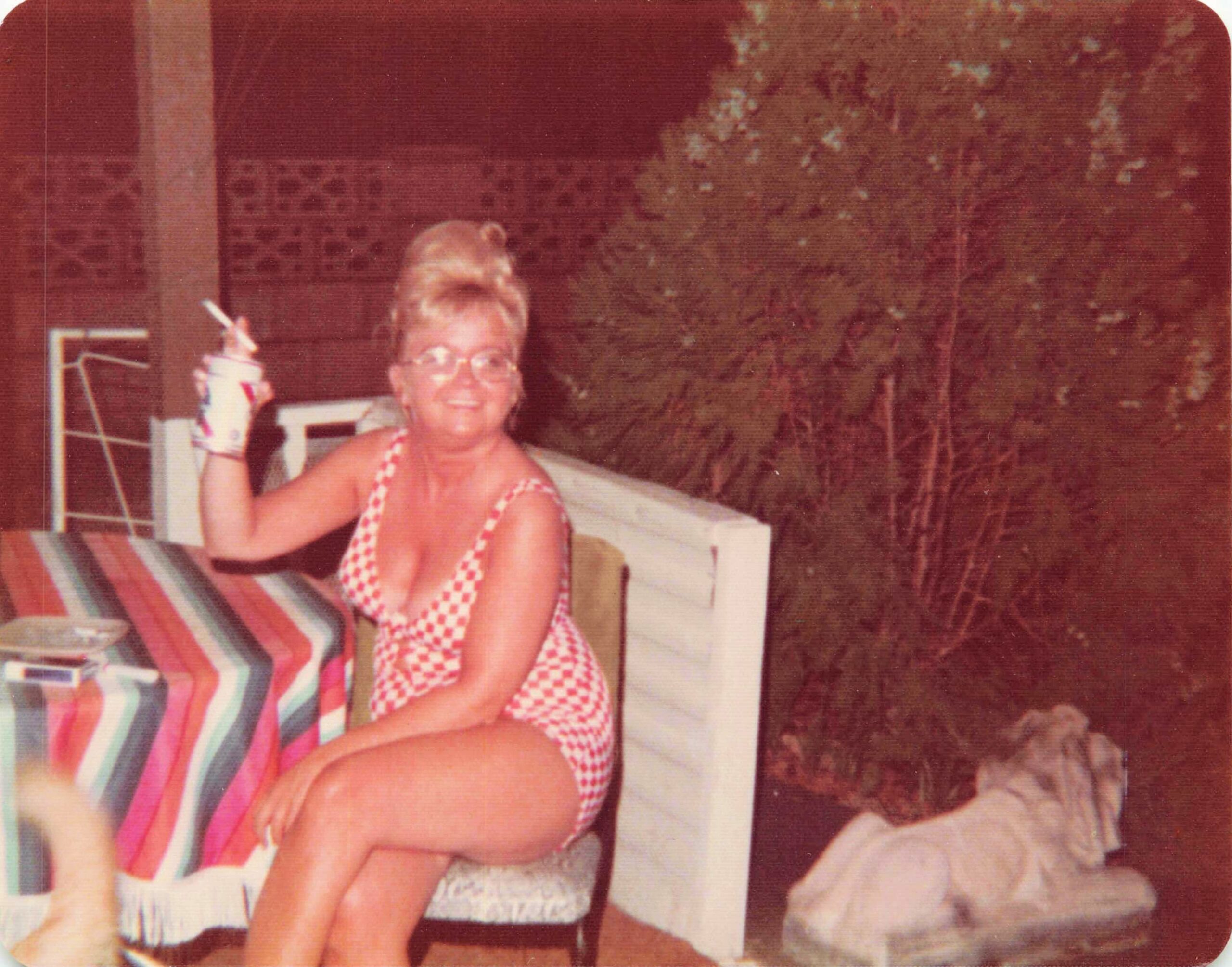 Smiling woman in a red-and-white checkered swimsuit standing by a poolside area.