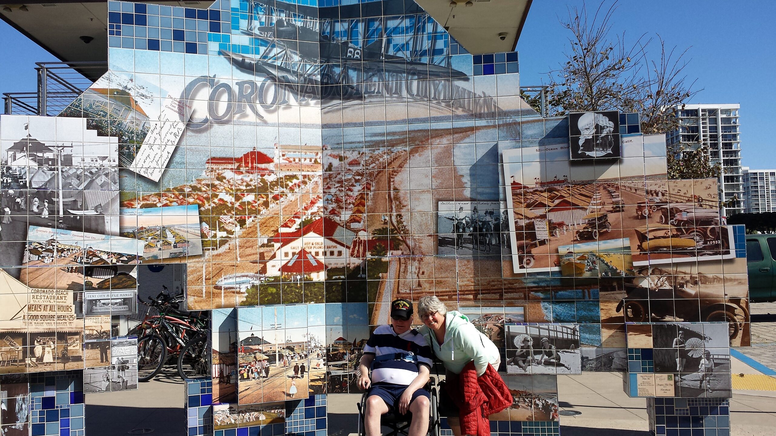 Colorful tiled mural collage of Coronado history, made from small photos in blue and beige tiles, with two people posing in front.