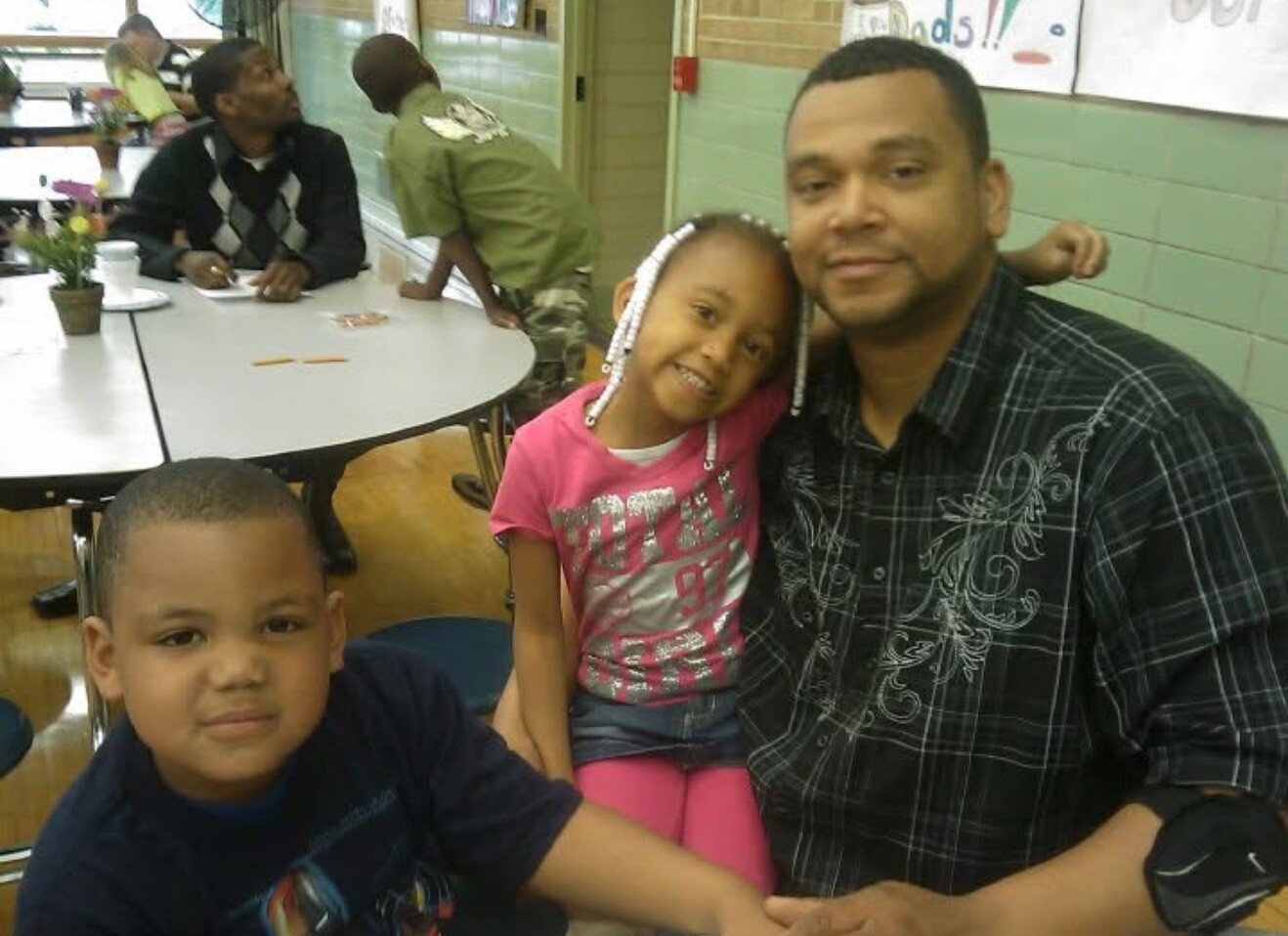 Man sitting with two children at a cafeteria table, smiling for the camera.