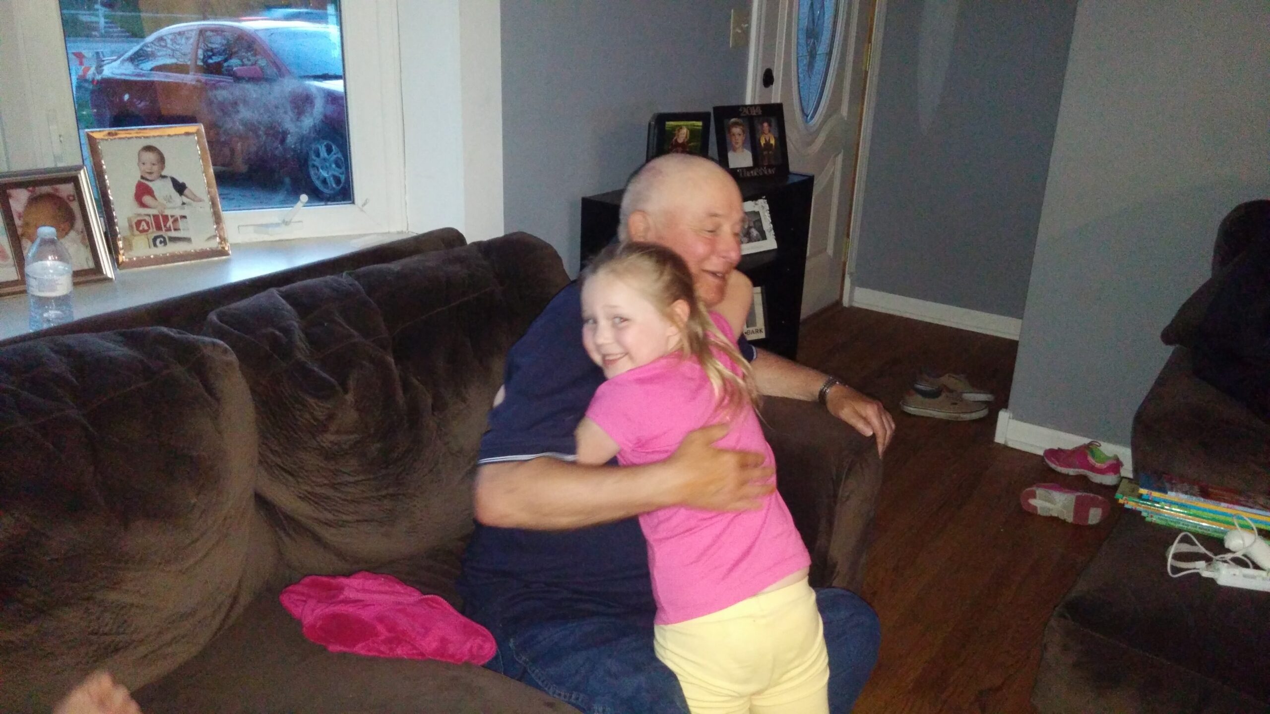 An older man on a brown sofa hugging two smiling children in a living room.
