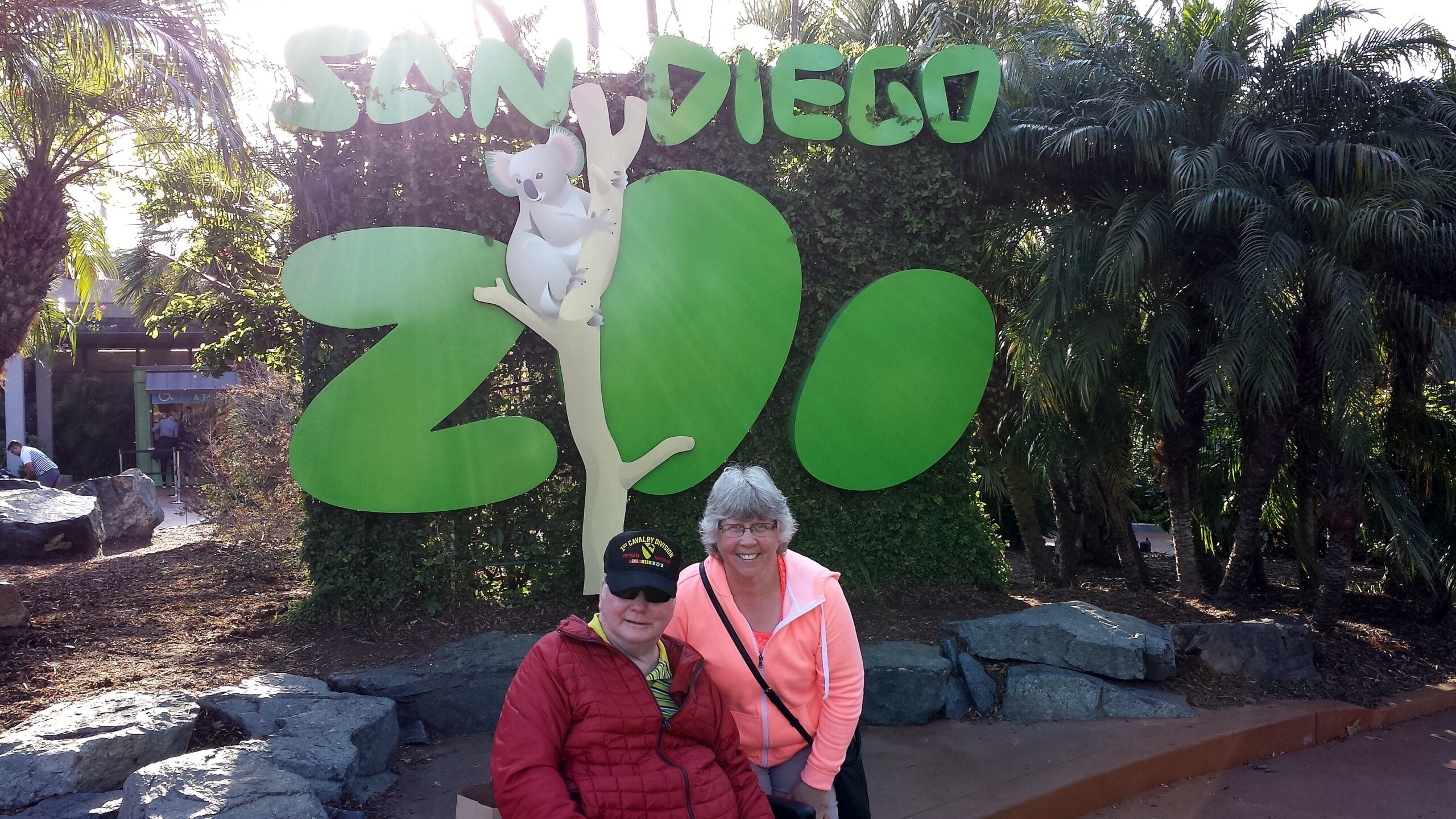 Two smiling women posing in front of a large green '200' sculpture with a koala cutout at the San Diego Zoo.