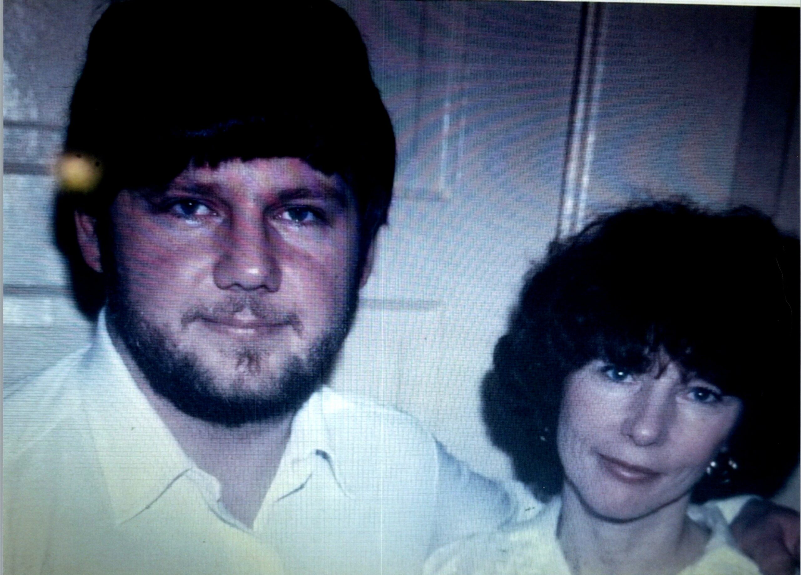 Man with dark hair and beard in a light shirt, posing with a woman who has short dark hair and a necklace in a close-up photo.