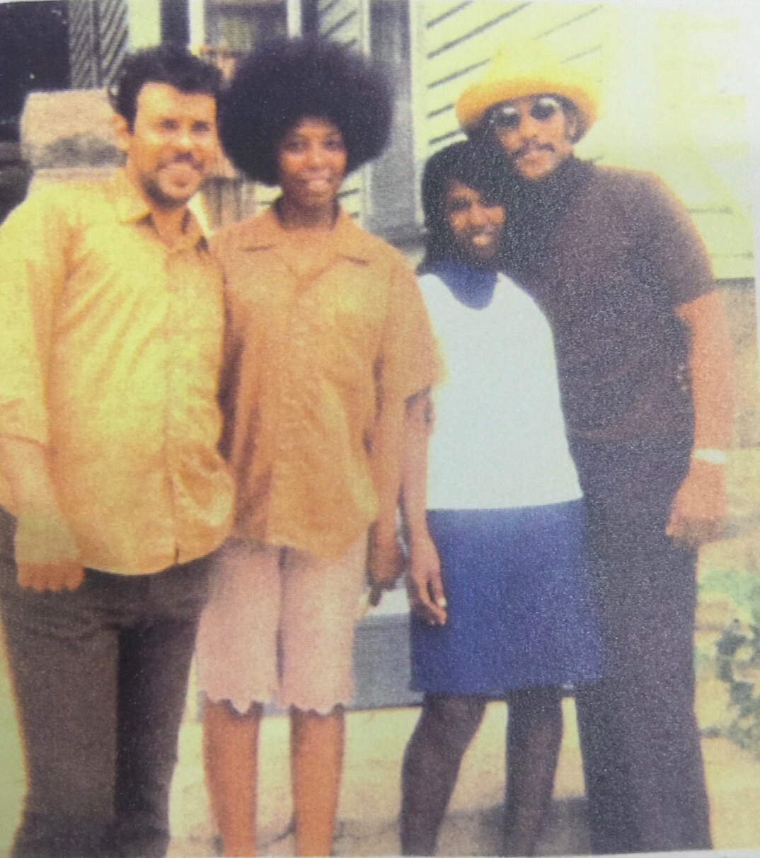 Four people posing outdoors for a photo: two men, a woman with an Afro, and a girl in a white shirt.