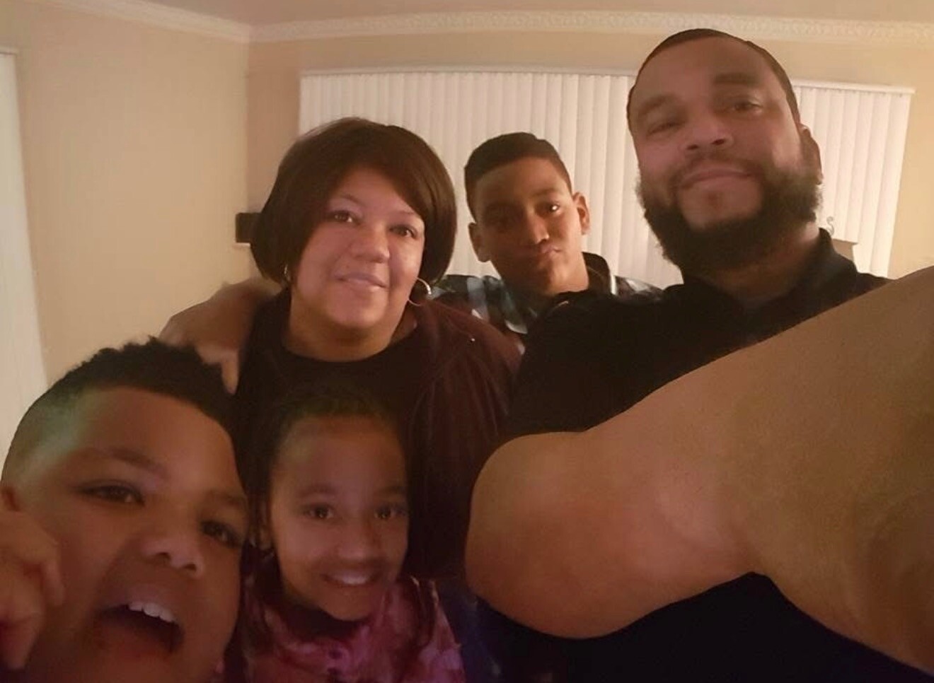 A family of five taking a selfie in a living room, smiling at the camera (man with beard on the right).