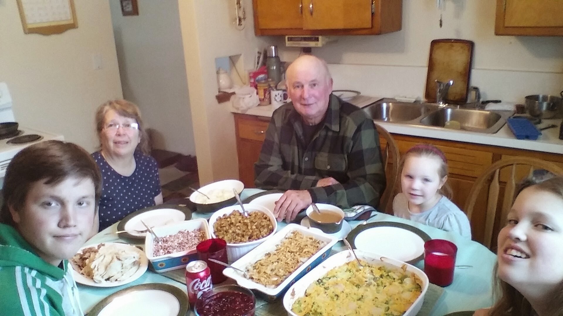 Family around a dining table in a kitchen, bowls of pasta and side dishes, smiling for the camera.