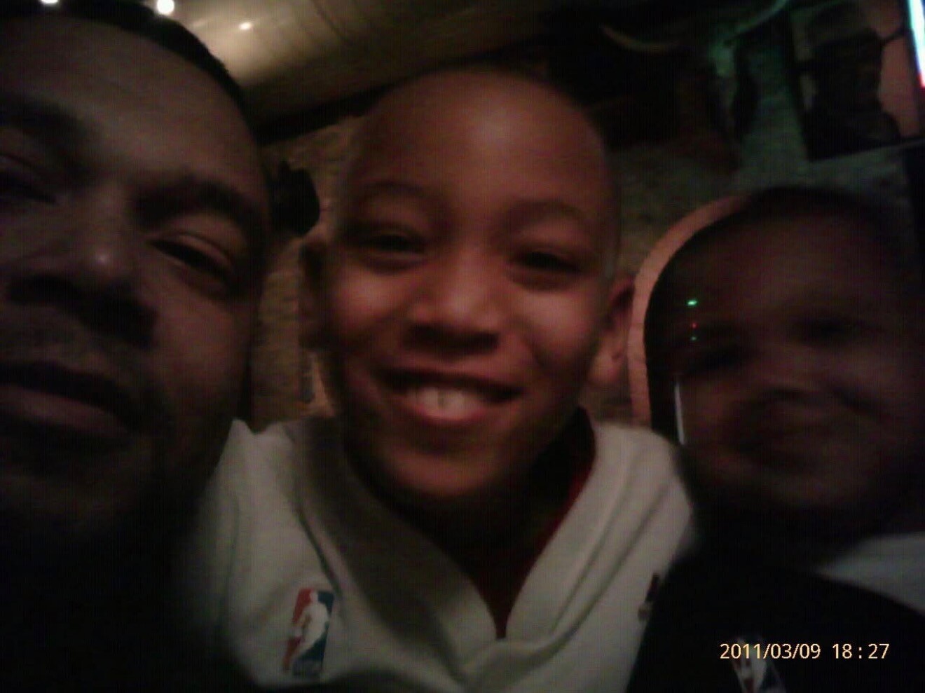 Three people lean in close for a low-light selfie, smiling at the camera in a dim room.