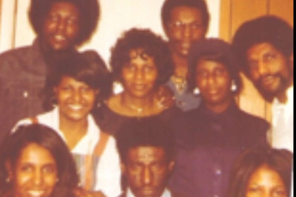 Group of diverse friends posing together for a casual, warmly lit 1970s-era photo.