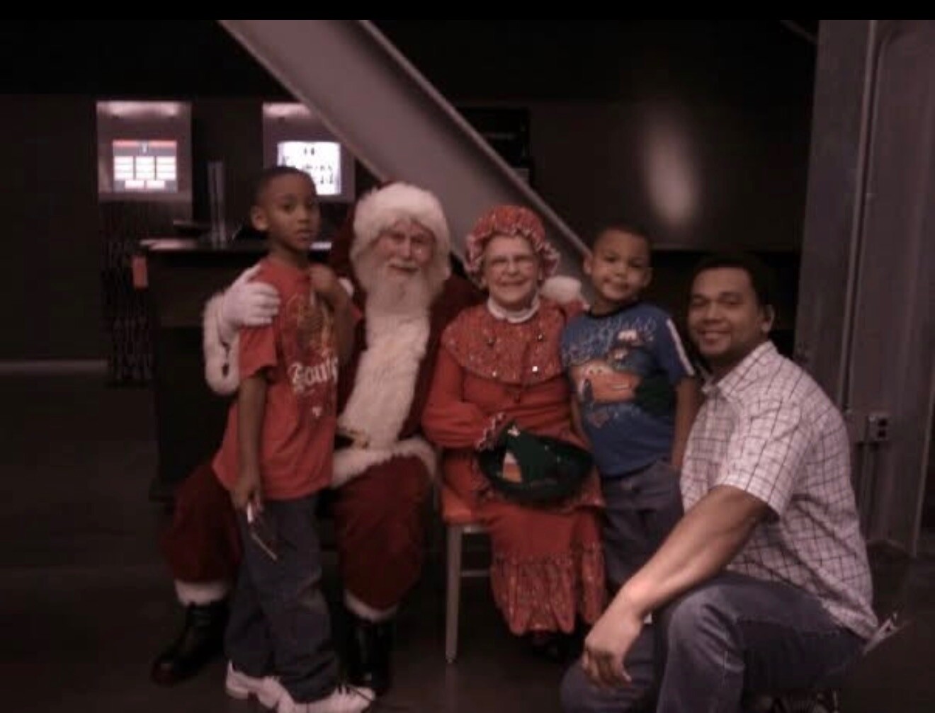 Family group photo with Santa Claus and Mrs. Claus, two young boys, and a man posing indoors.