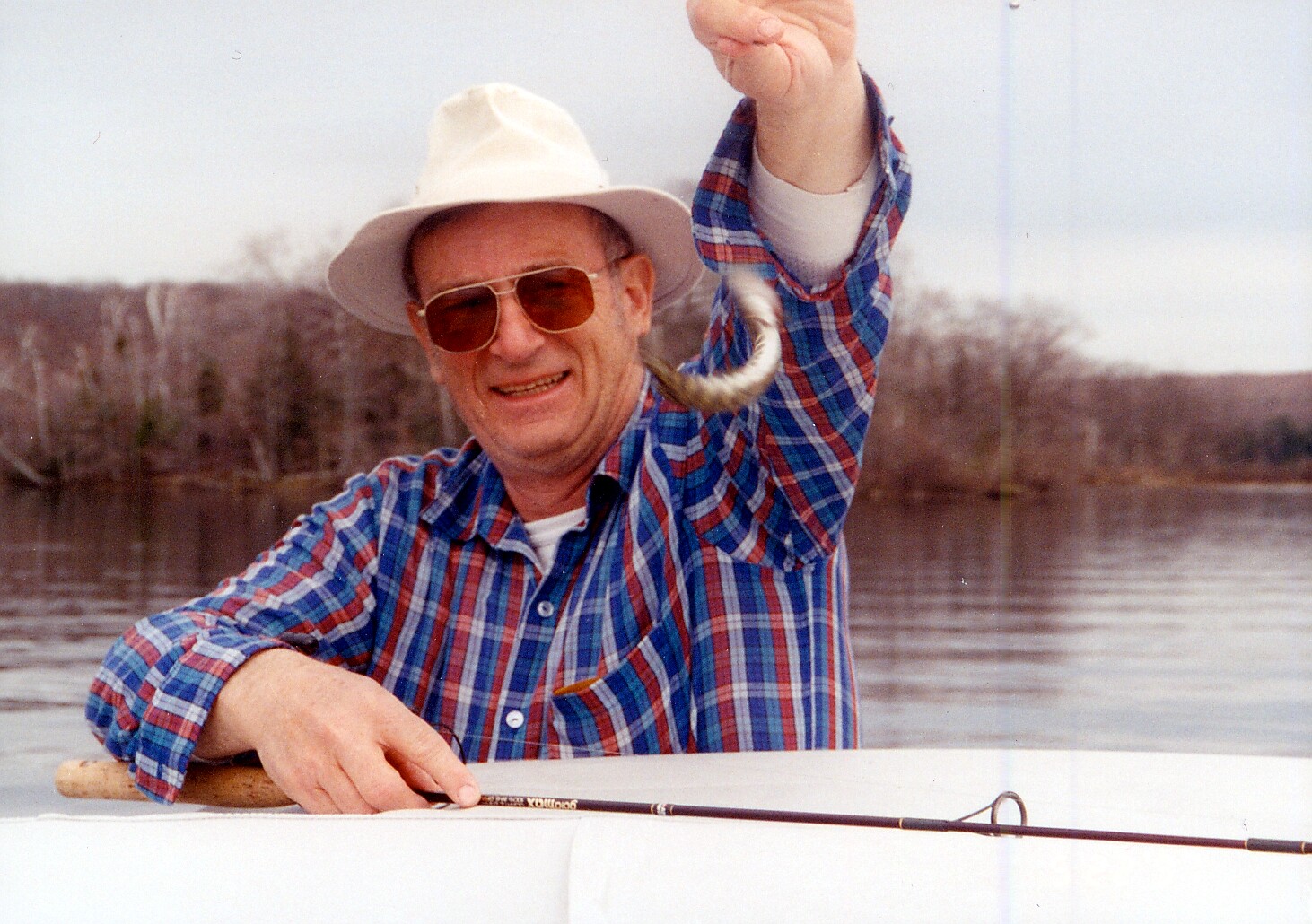 Smiling man in a white hat and sunglasses on a boat, holding up a small fish he just caught while fishing on a lake.