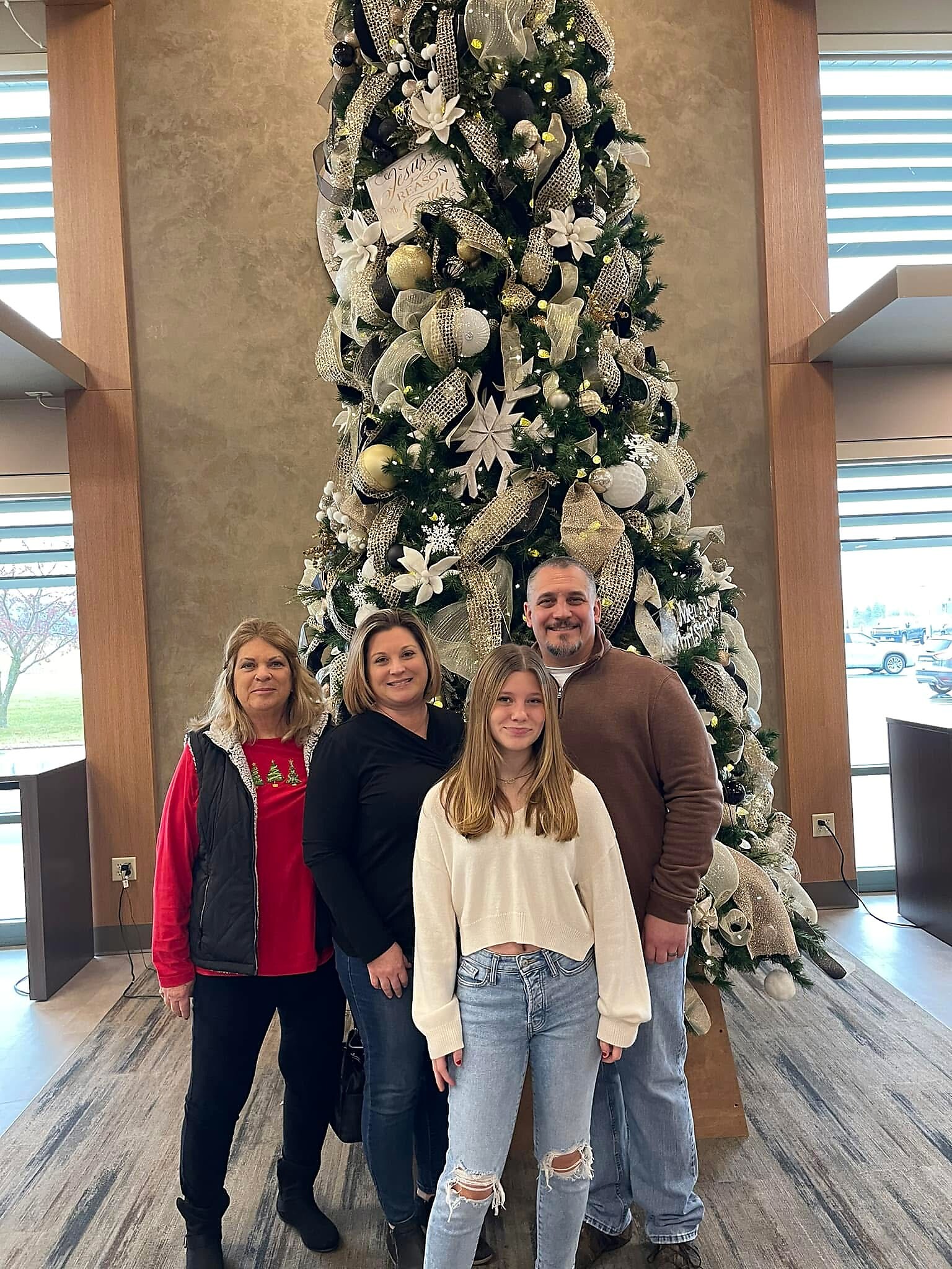 Group of five people posing in front of a large, white-and-silver Christmas tree inside a building lobby.