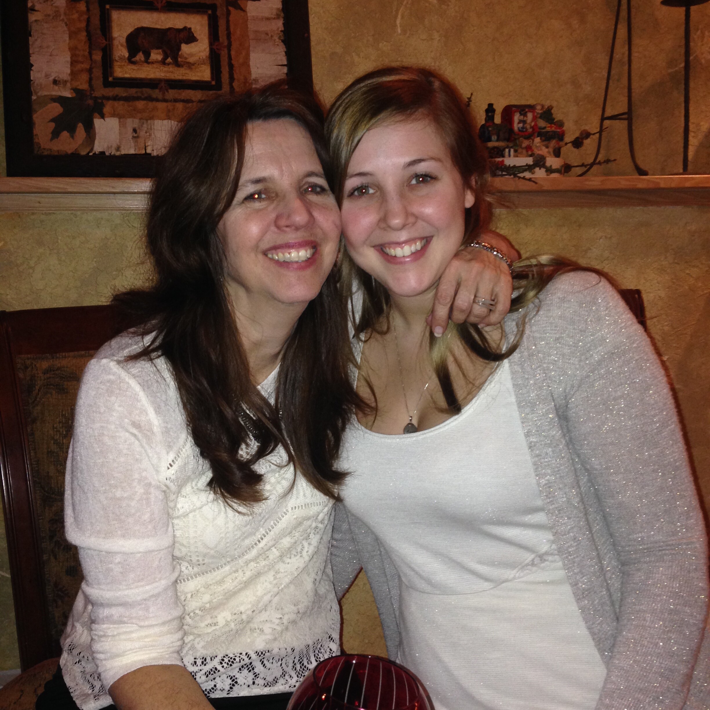 Two women smiling at the camera in a restaurant, seated close together, with a wine glass in the foreground.
