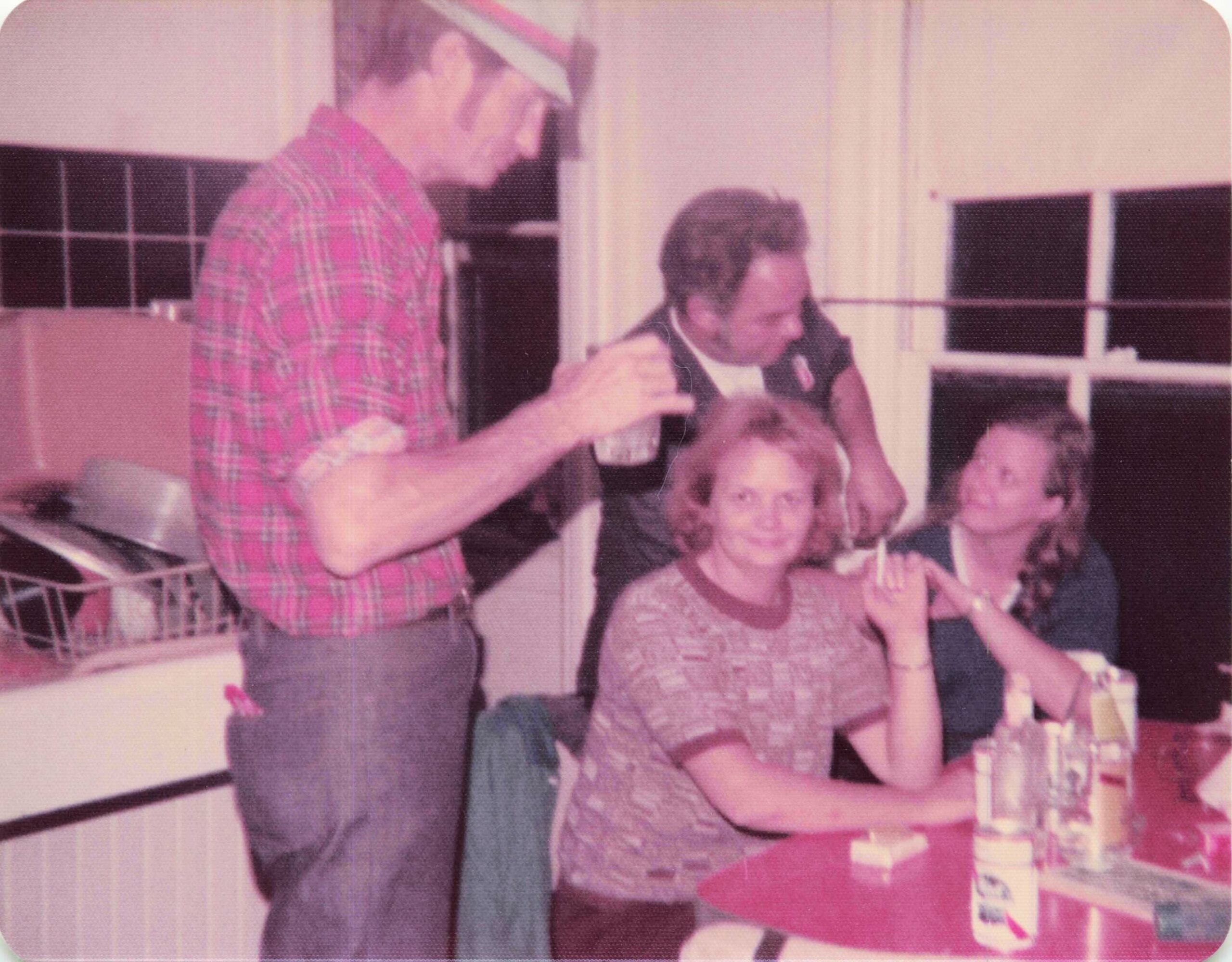 Man in a pink plaid shirt stands beside a seated woman and two children at a store counter.
