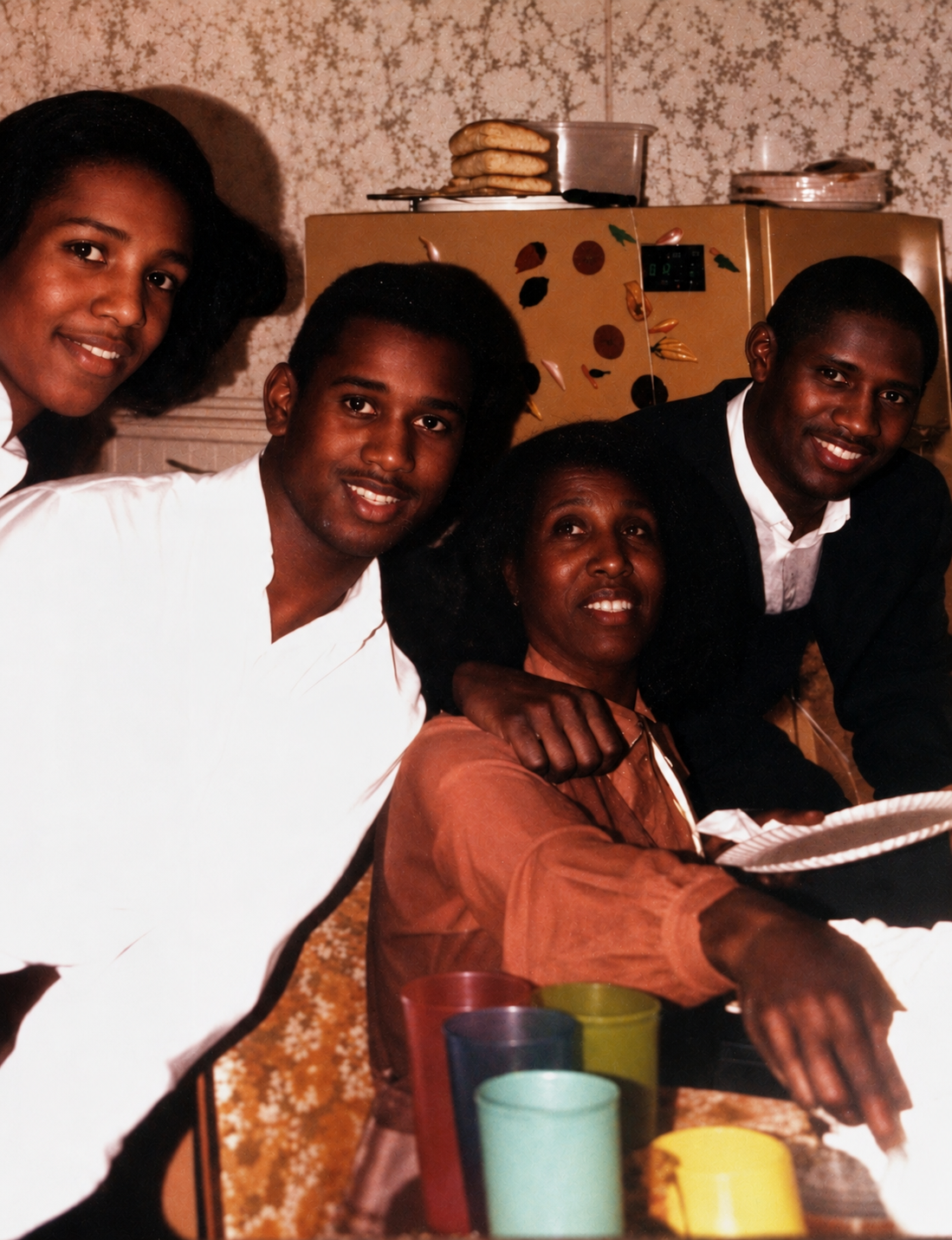 Four people gathered around a dining table in a kitchen, smiling at the camera with colorful plastic cups on the table behind them
