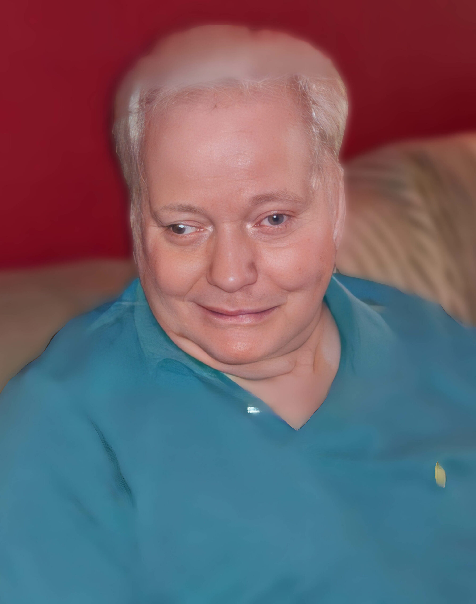 Close-up portrait of a person with short white hair wearing a teal shirt, against a red background.