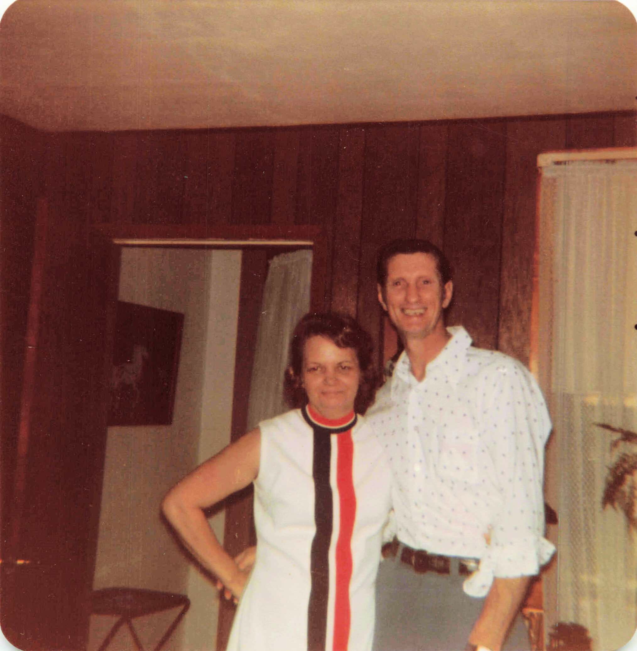 Two people pose indoors in a home setting; one wears a white shirt with a bold red vertical stripe while another stands nearby.