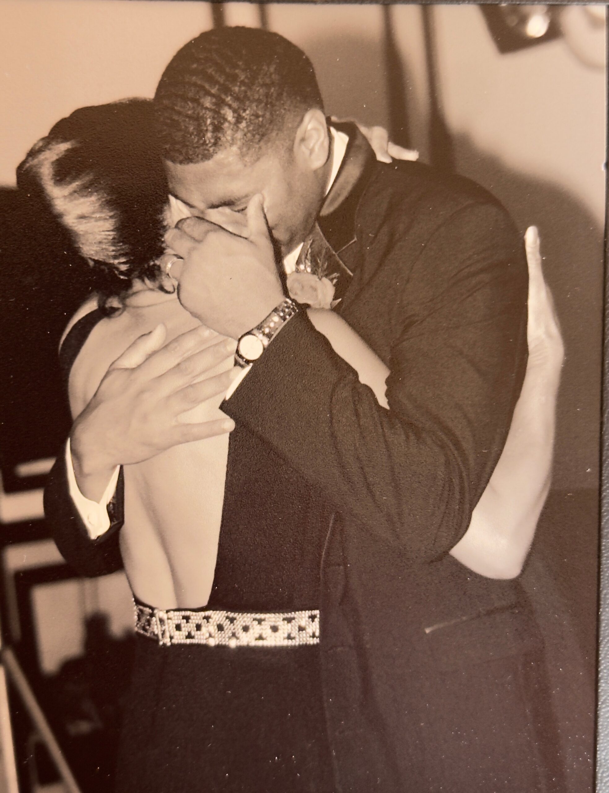 A couple sharing a kiss and hug, the man in a suit and patterned belt.