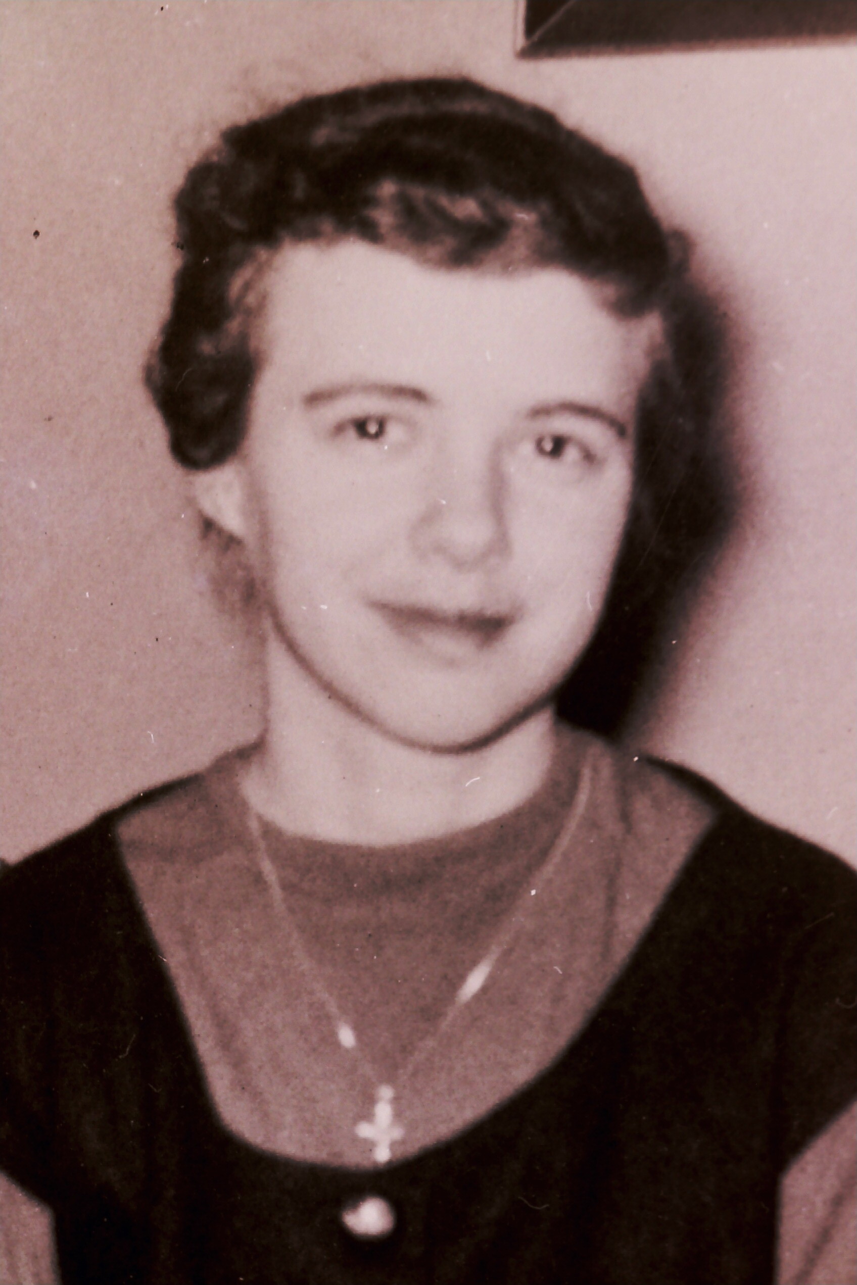 Sepia-toned portrait of a young woman with short dark hair, wearing a dark sweater over a blouse and a small cross necklace.
