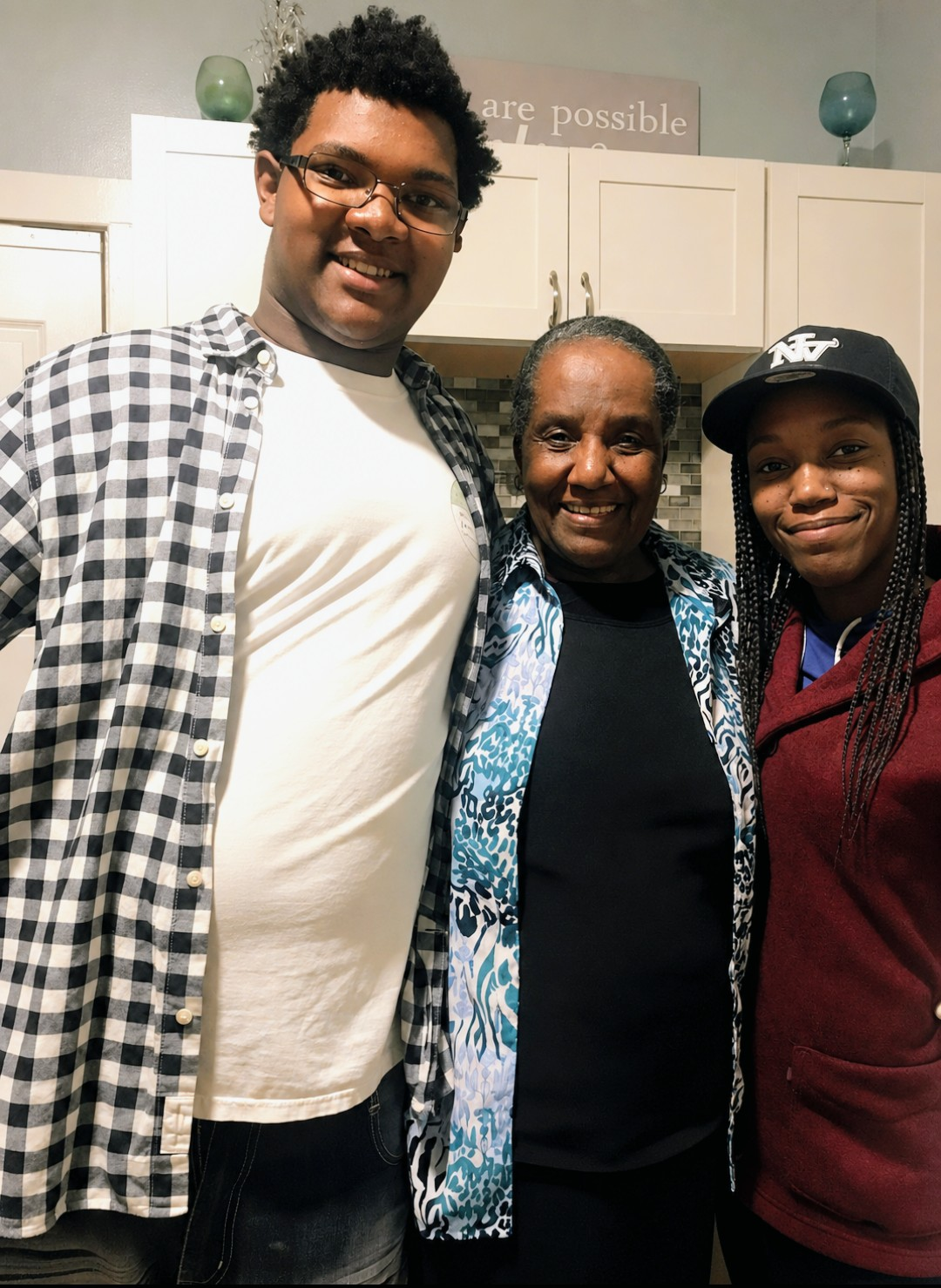 Three people stand together in a kitchen, smiling at the camera (young man on left, older woman in middle, young woman on right).