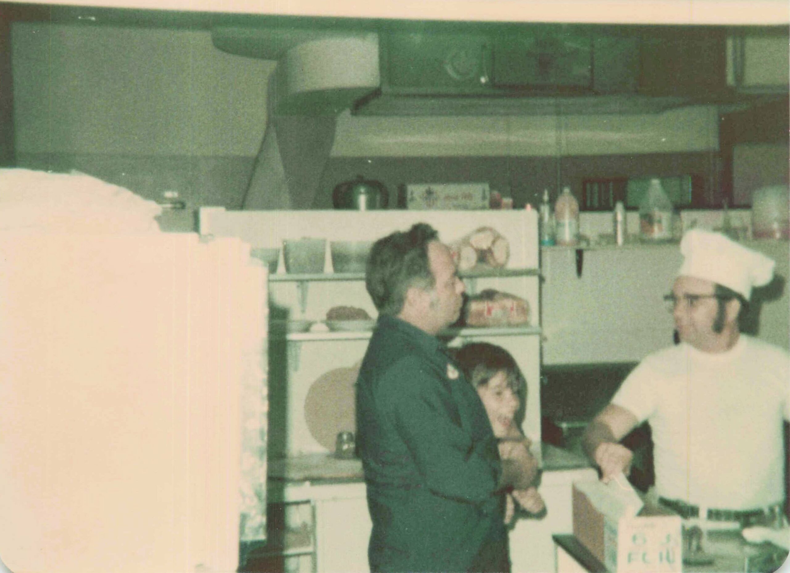 Two people at a store counter, with shelves of items behind them in a dim, vintage photo.