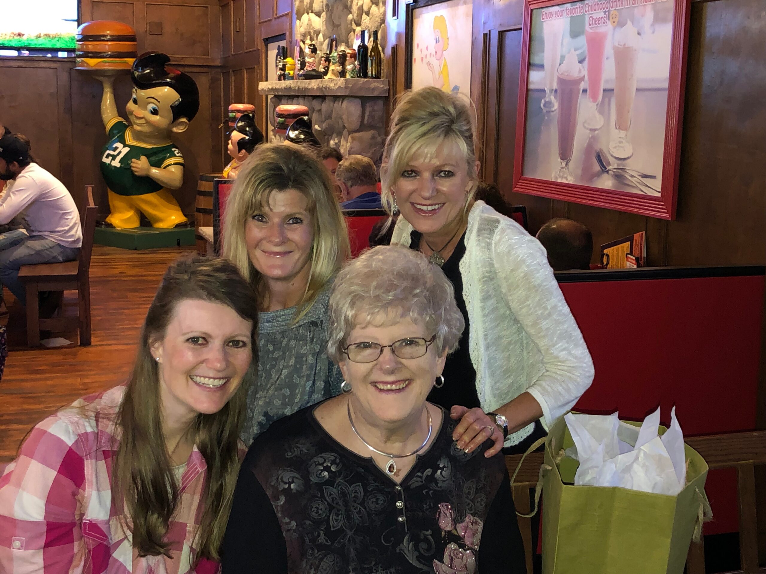 Group of women smiling for a photo in a retro restaurant, with a giant cartoon boy statue holding a hamburger in the background.