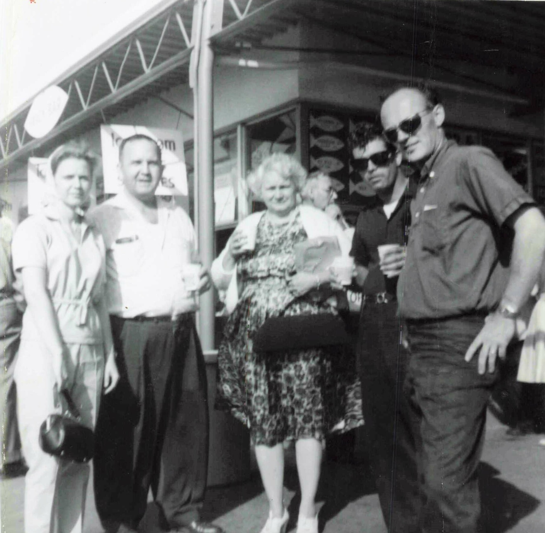 Group of five adults posing outside a shop, smiling at the camera.