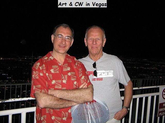 Two men pose on a balcony at night with Las Vegas lights in the distance; one wears a red Hawaiian shirt with arms crossed, the other a gray 'Las Vegas' t-shirt with sunglasses tucked in. Caption above reads 'Art & CW in Vegas'.