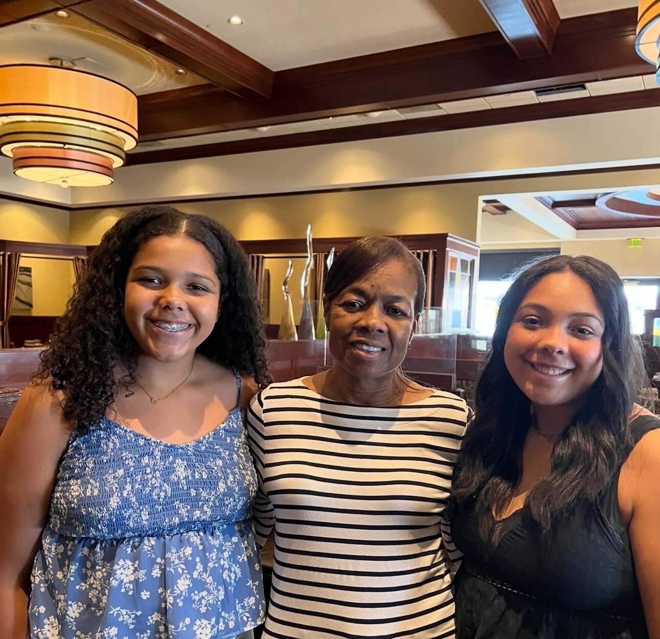 Three smiling women posing together in a restaurant setting with warm lighting.