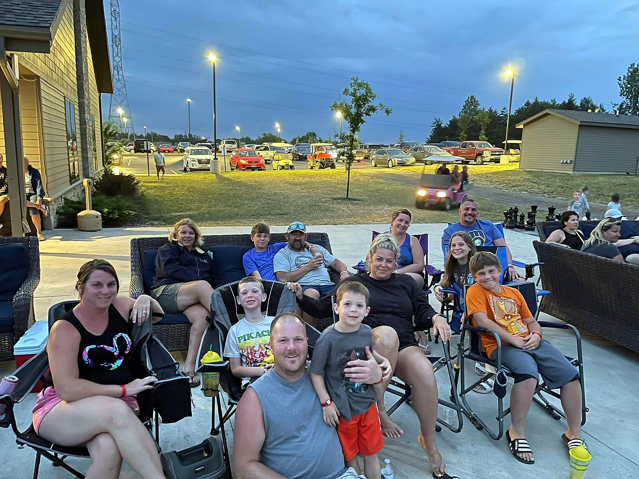 Group of family and friends smiling and seated in lawn chairs at an evening outdoor gathering.