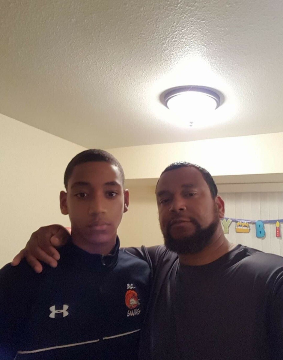 Two men pose for a selfie indoors, one with his arm around the other's shoulder, birthday banner in the background.