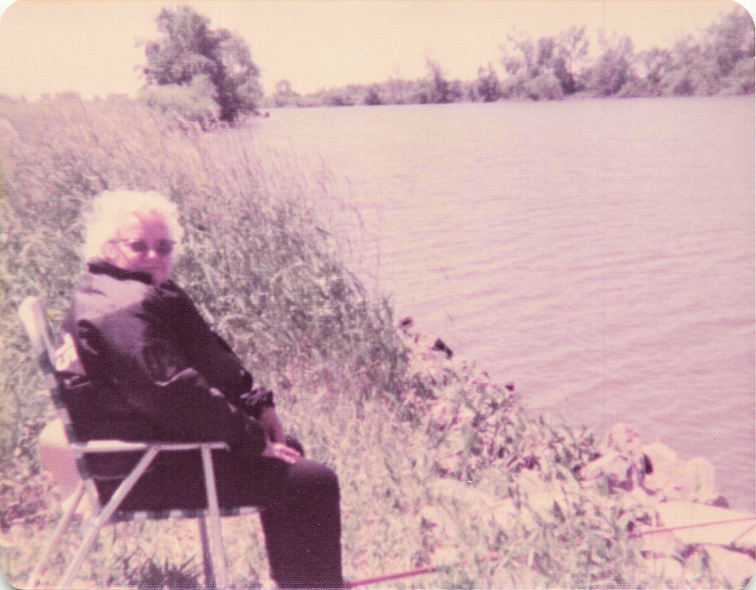 Older man standing beside a bicycle on a grassy, shrub-filled field with trees in the distance.