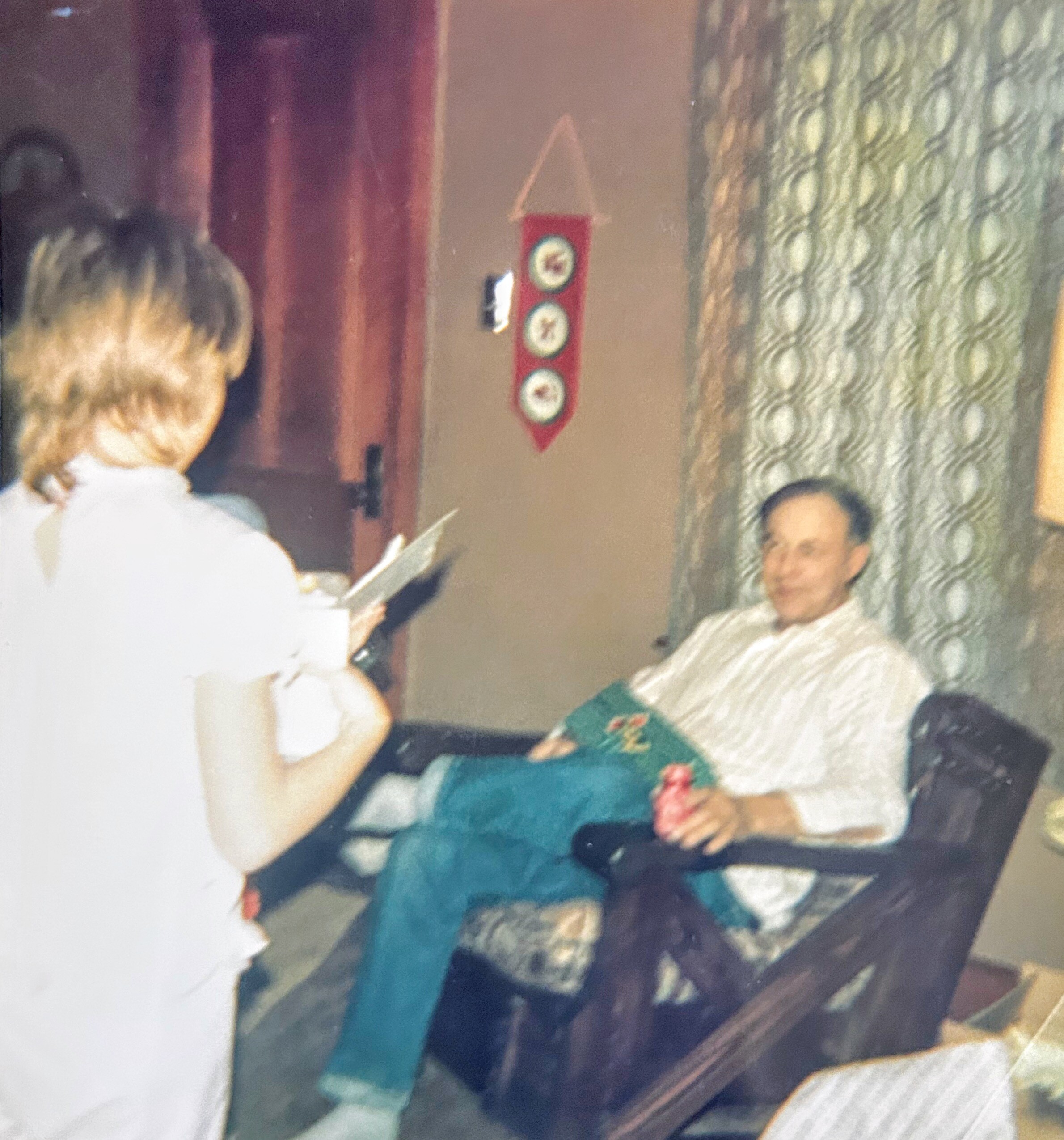 Blurry indoor scene with people seated around a table, facing a wall with a red hanging sign featuring circular symbols.