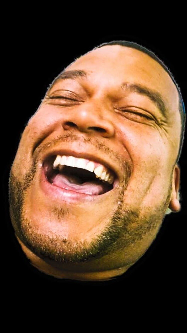 Close-up of a man laughing with mouth wide open against a black background, showing teeth and dimples.