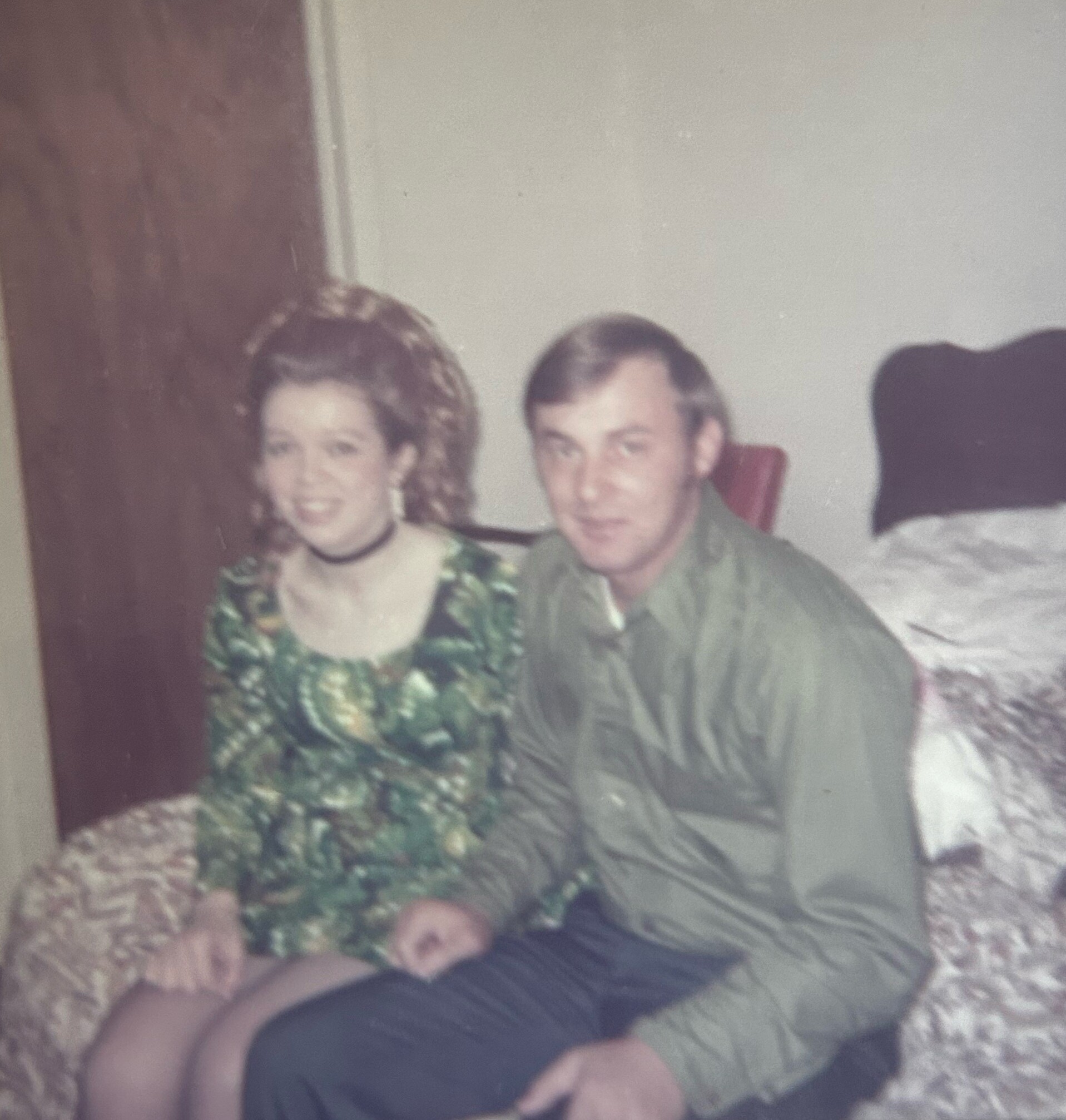 Blurry faded family photo: woman in a green floral dress and a man in a green shirt sit on a couch, with a child at the bottom edge.