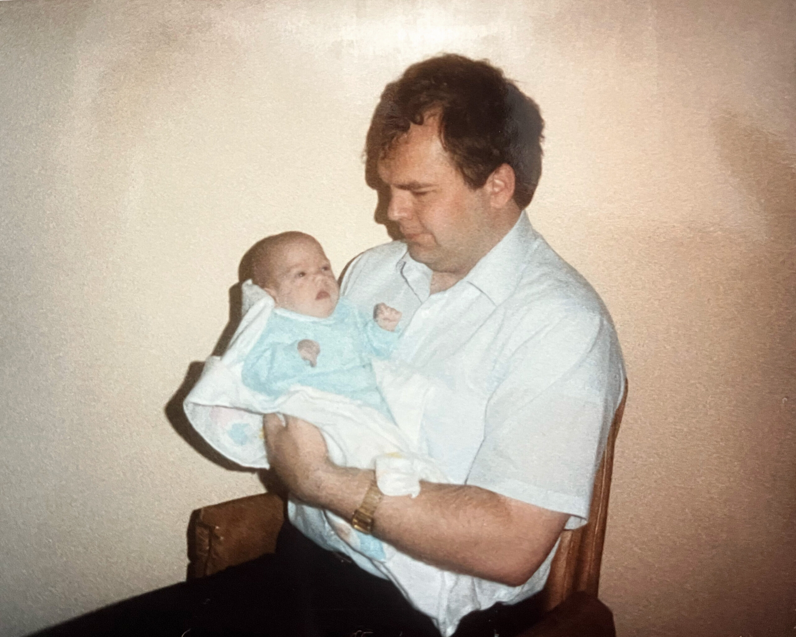 Man wearing a light shirt holding a newborn baby and looking down at the infant lovingly.