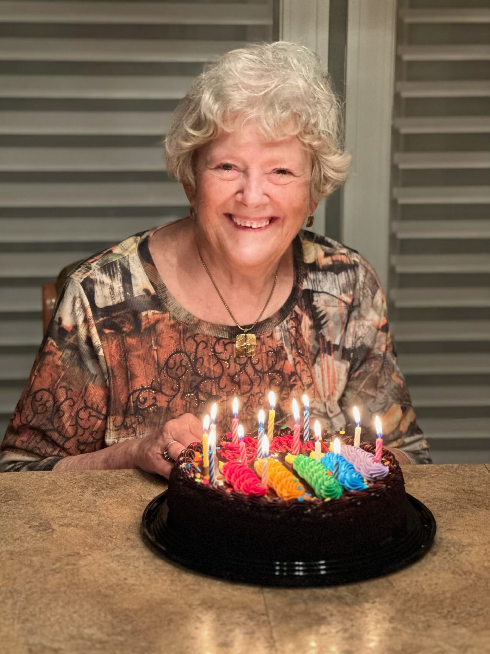 Smiling elderly woman at a birthday cake with lit candles in front of her.