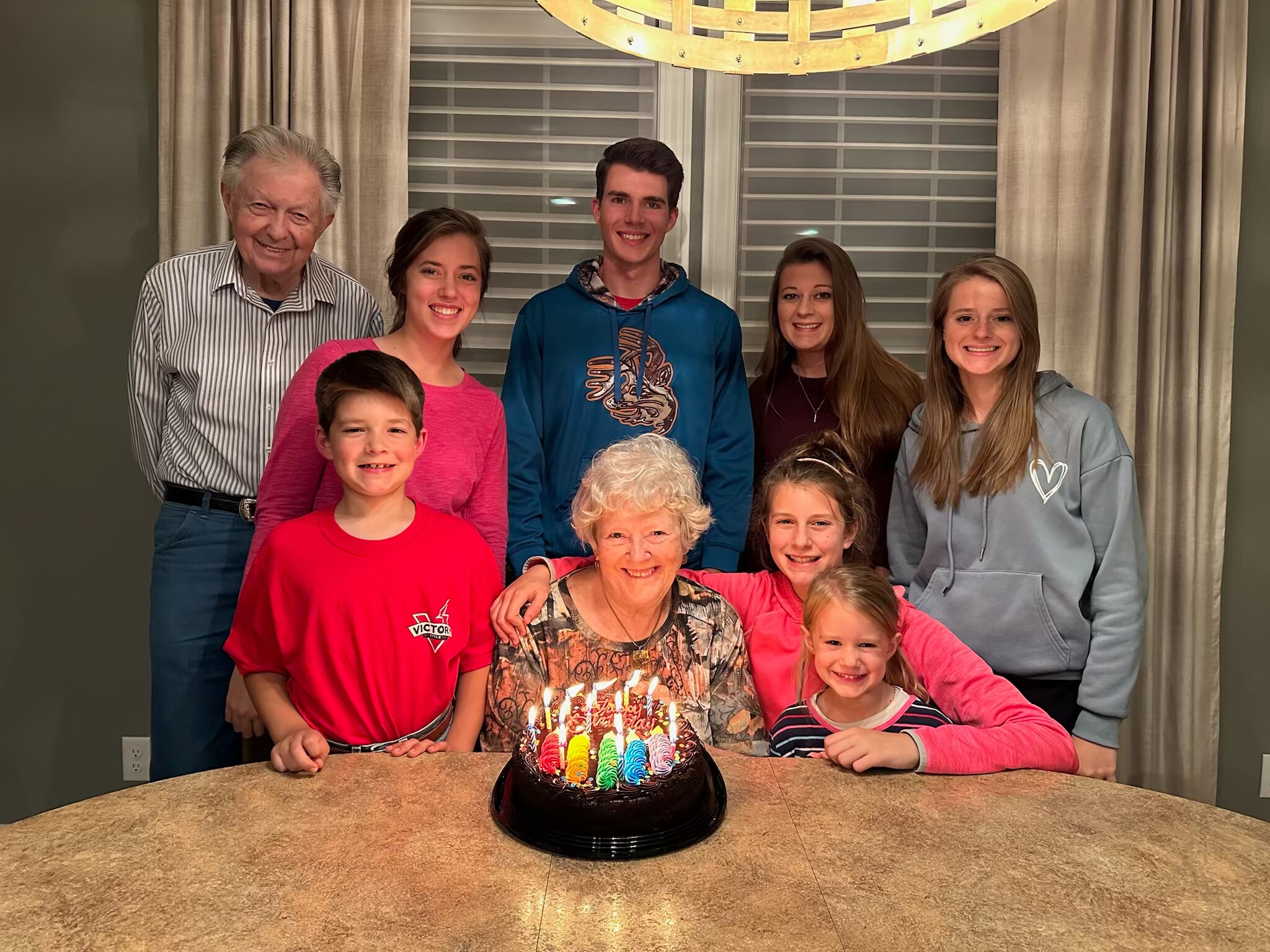 Group of family members posing behind a birthday cake with lit candles on a kitchen island or table indoors.