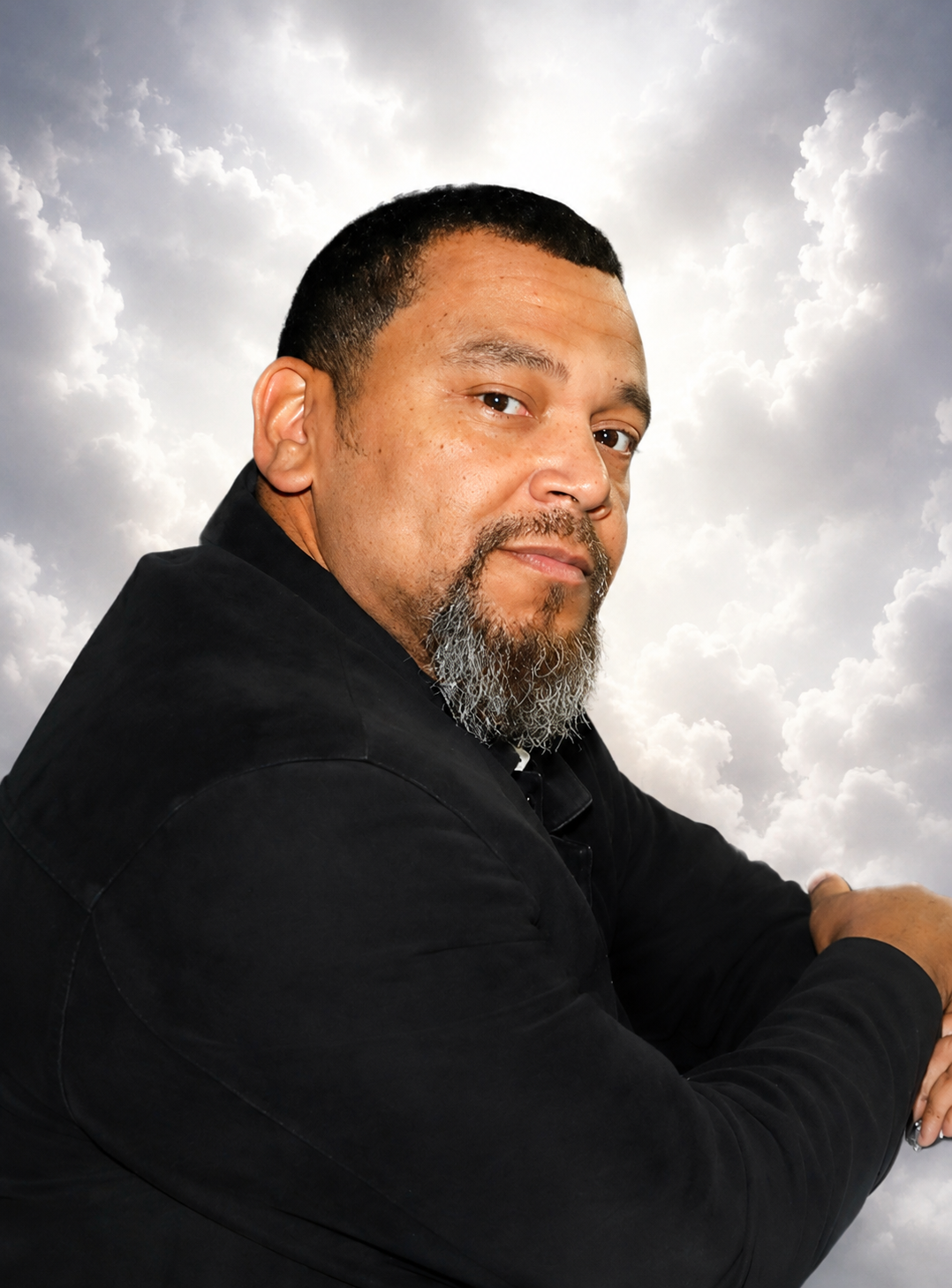 Portrait of a man with a short beard and mustache, wearing a black jacket, posed against a cloudy sky background.