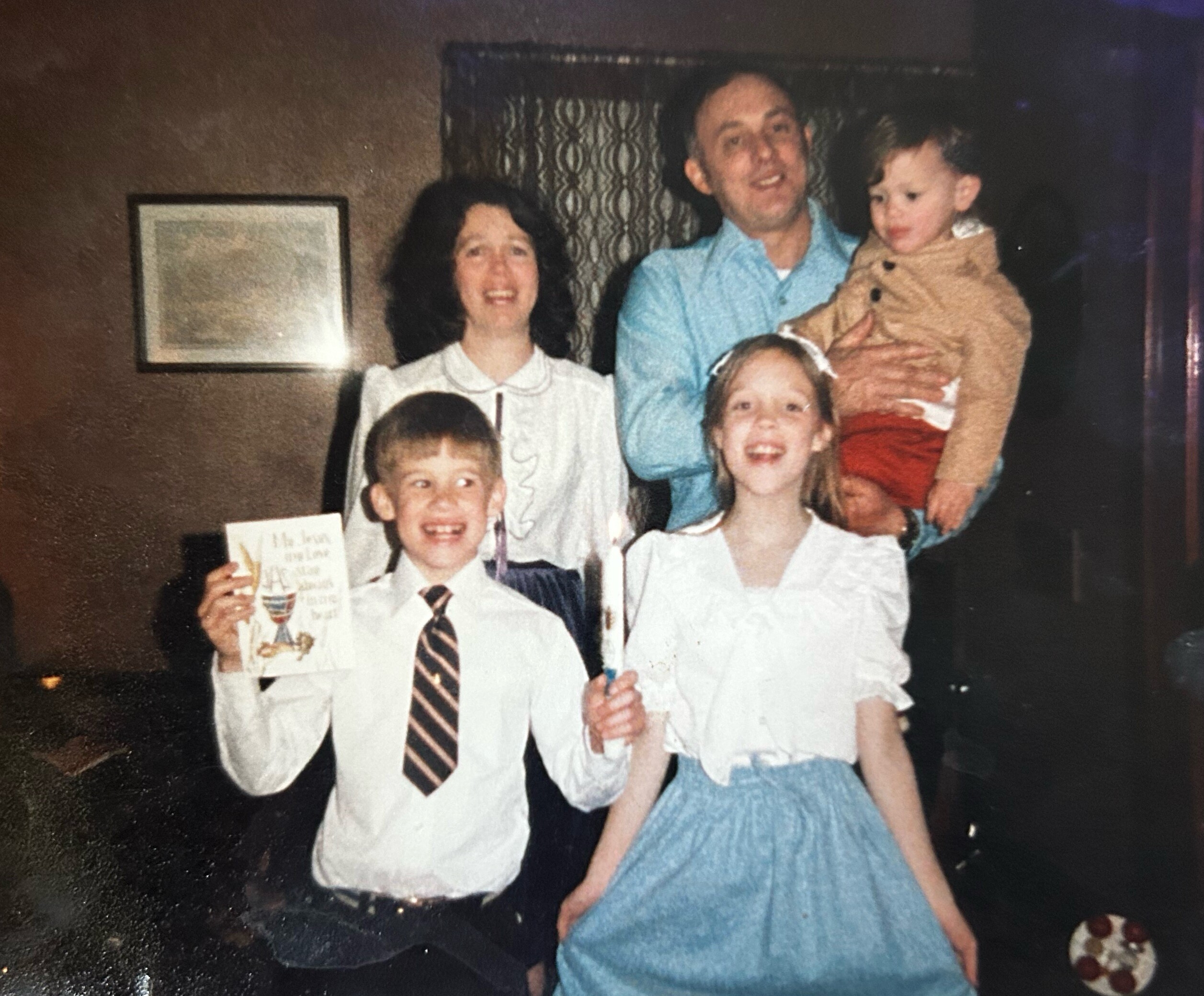 Family group photo in a living room: two adults with three children posing together, one adult holding a young child.