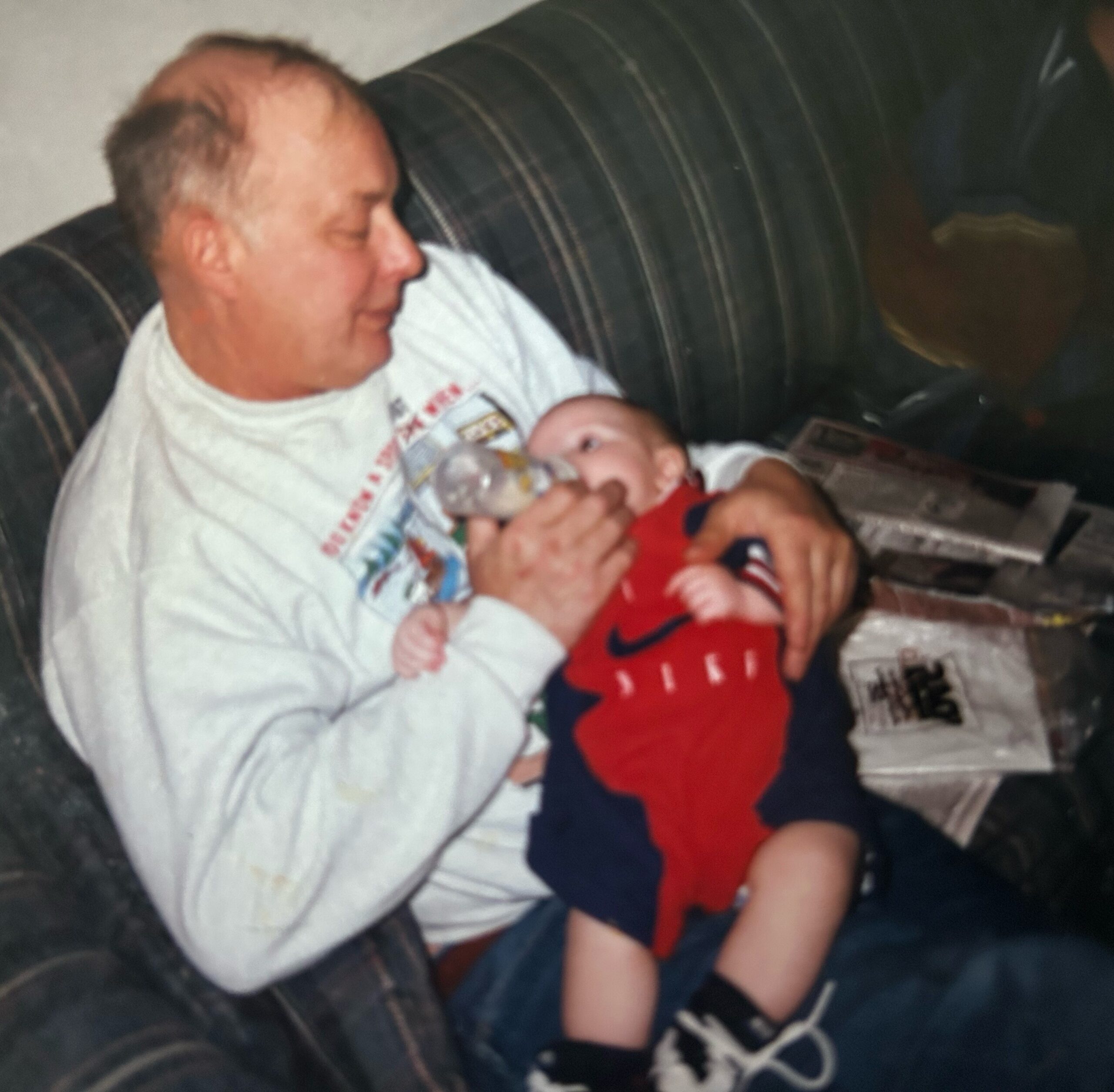 Man sitting on a dark striped sofa holding two newborn babies in his arms.