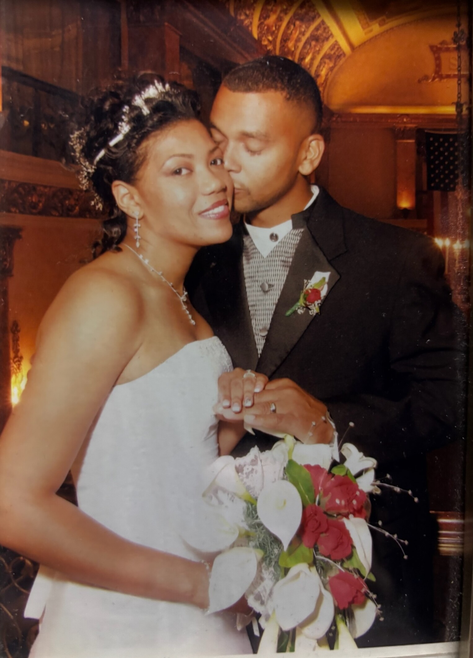 Bride and groom sharing a kiss on their wedding day, the bride holding a white bouquet with red accents in foreground.