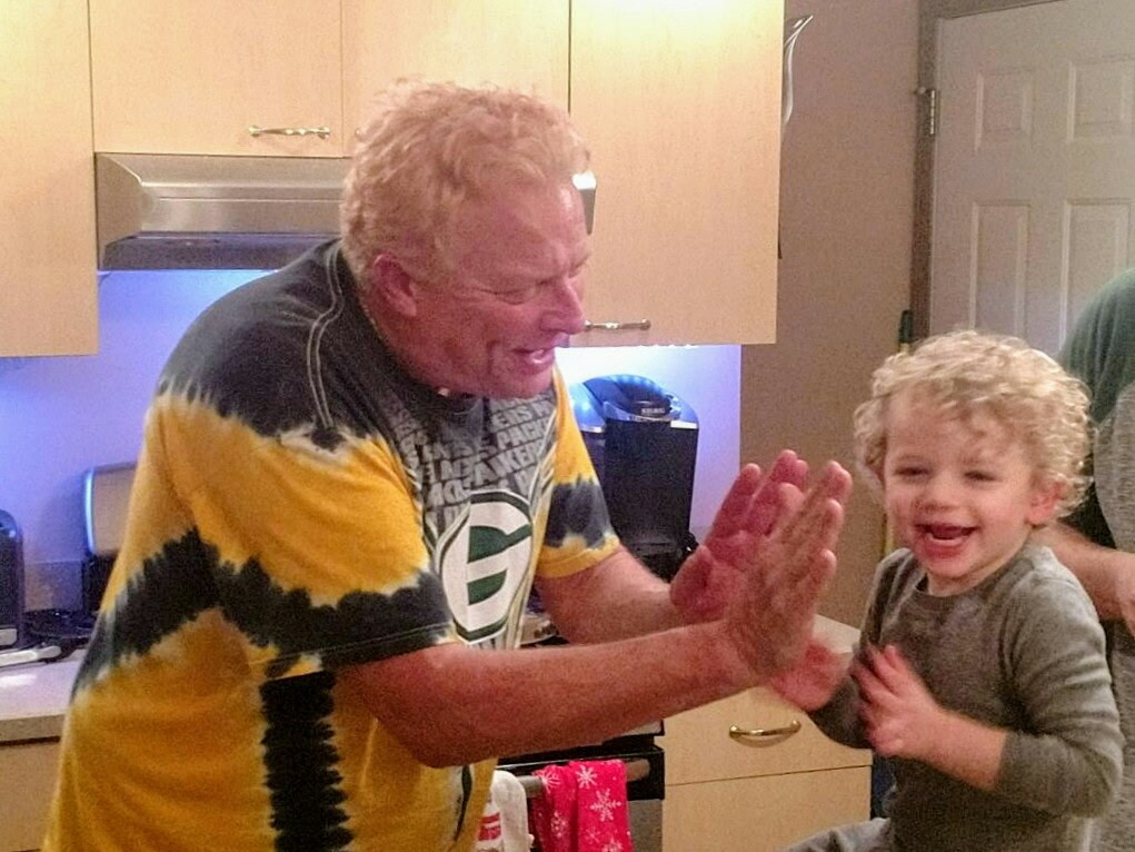 A smiling man and a young boy give each other a high-five in a kitchen.