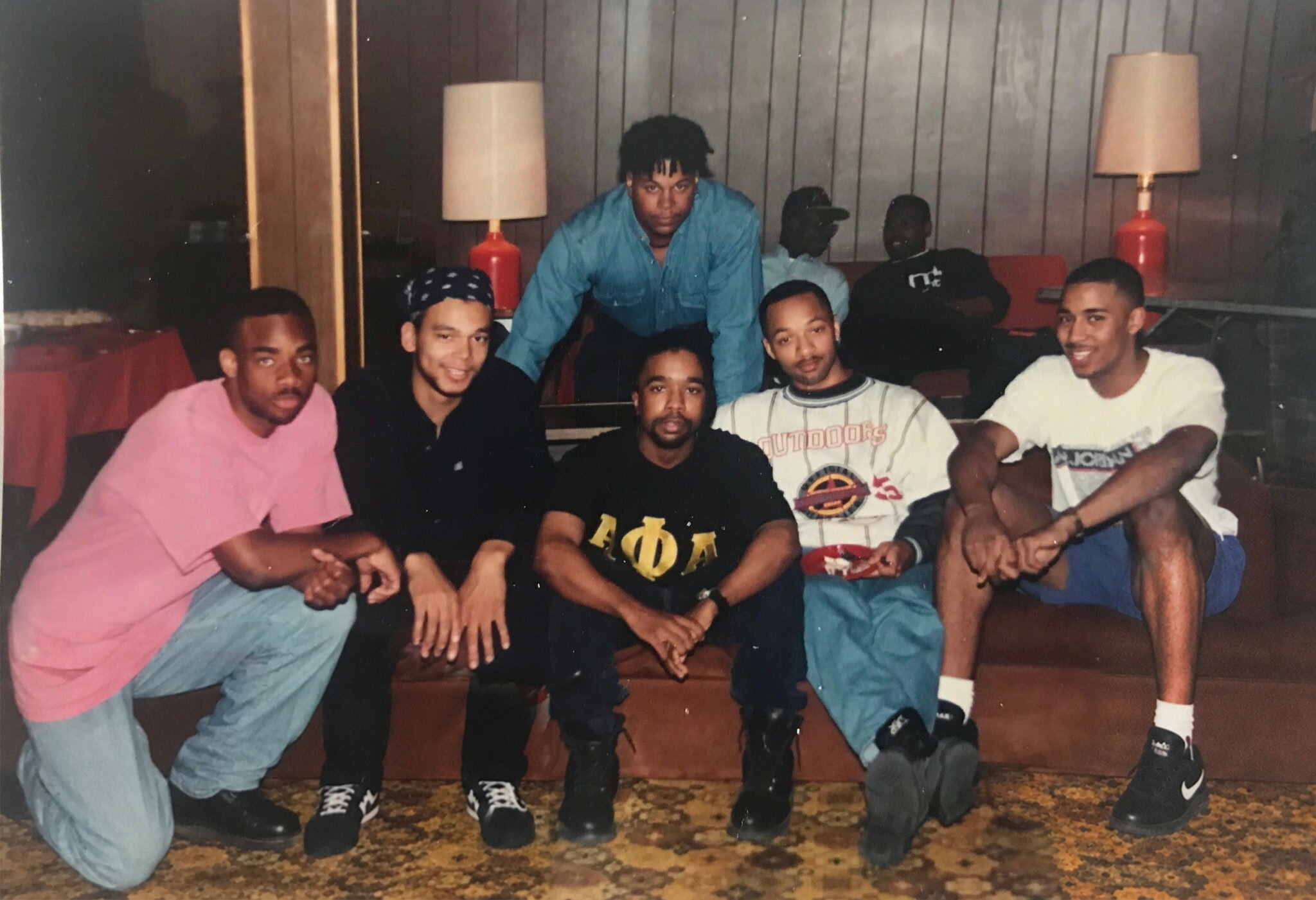 Group of young men posing together in a casual room, leaning in and smiling for the photo.