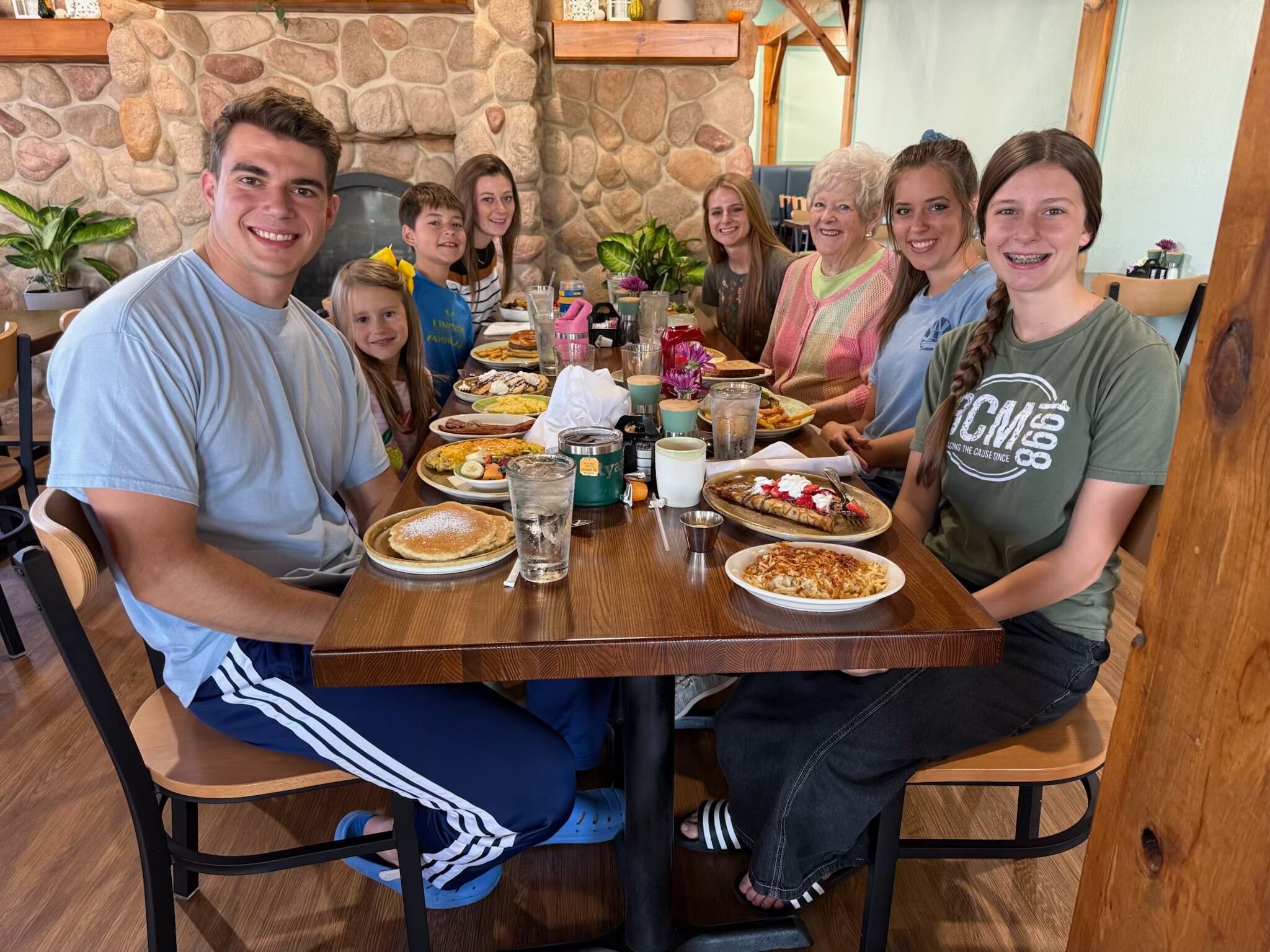 Group of ten people sitting around a wooden table in a cozy stone-walled restaurant, smiling at the camera.