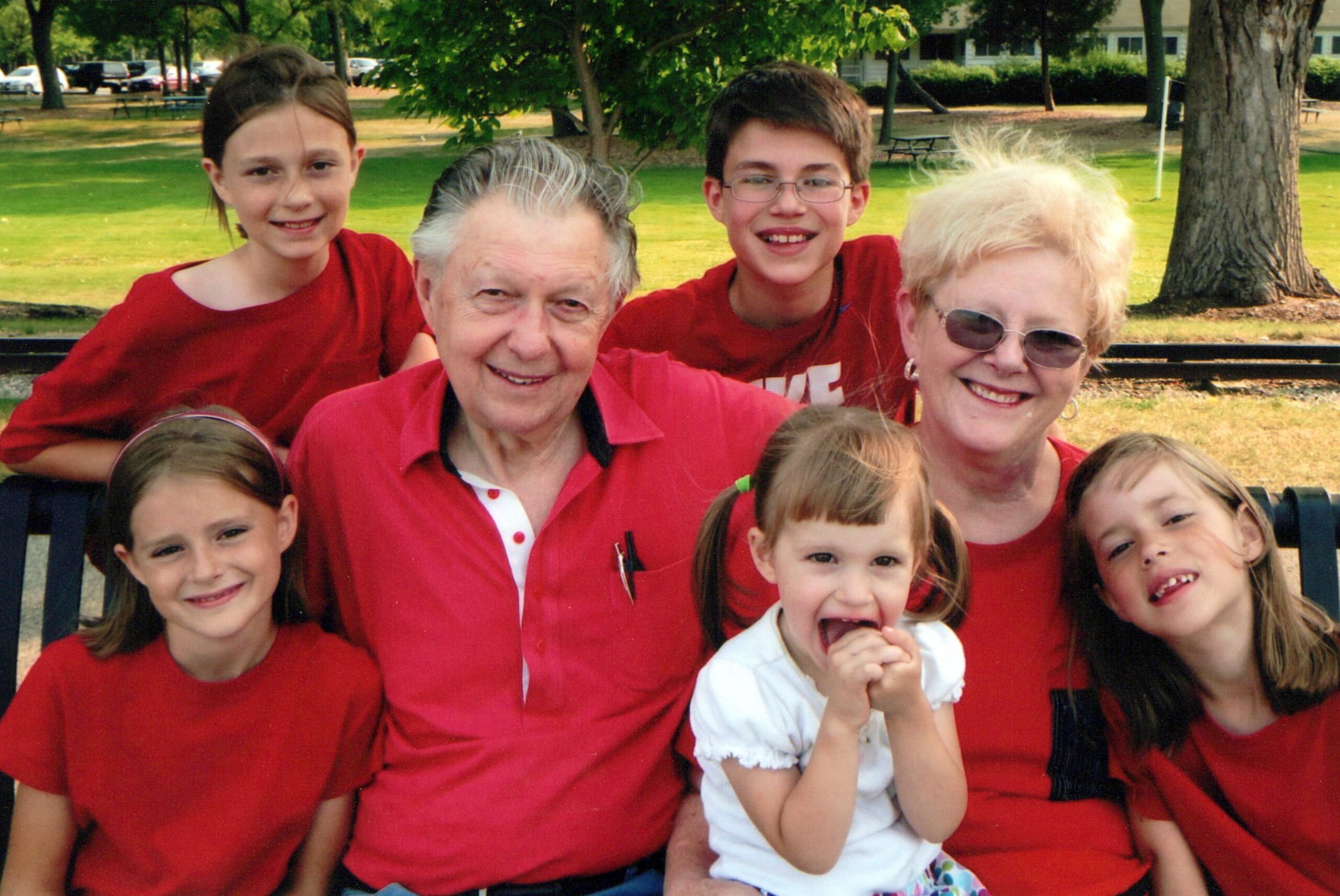Smiling family group in red shirts posing on a bench in a park.