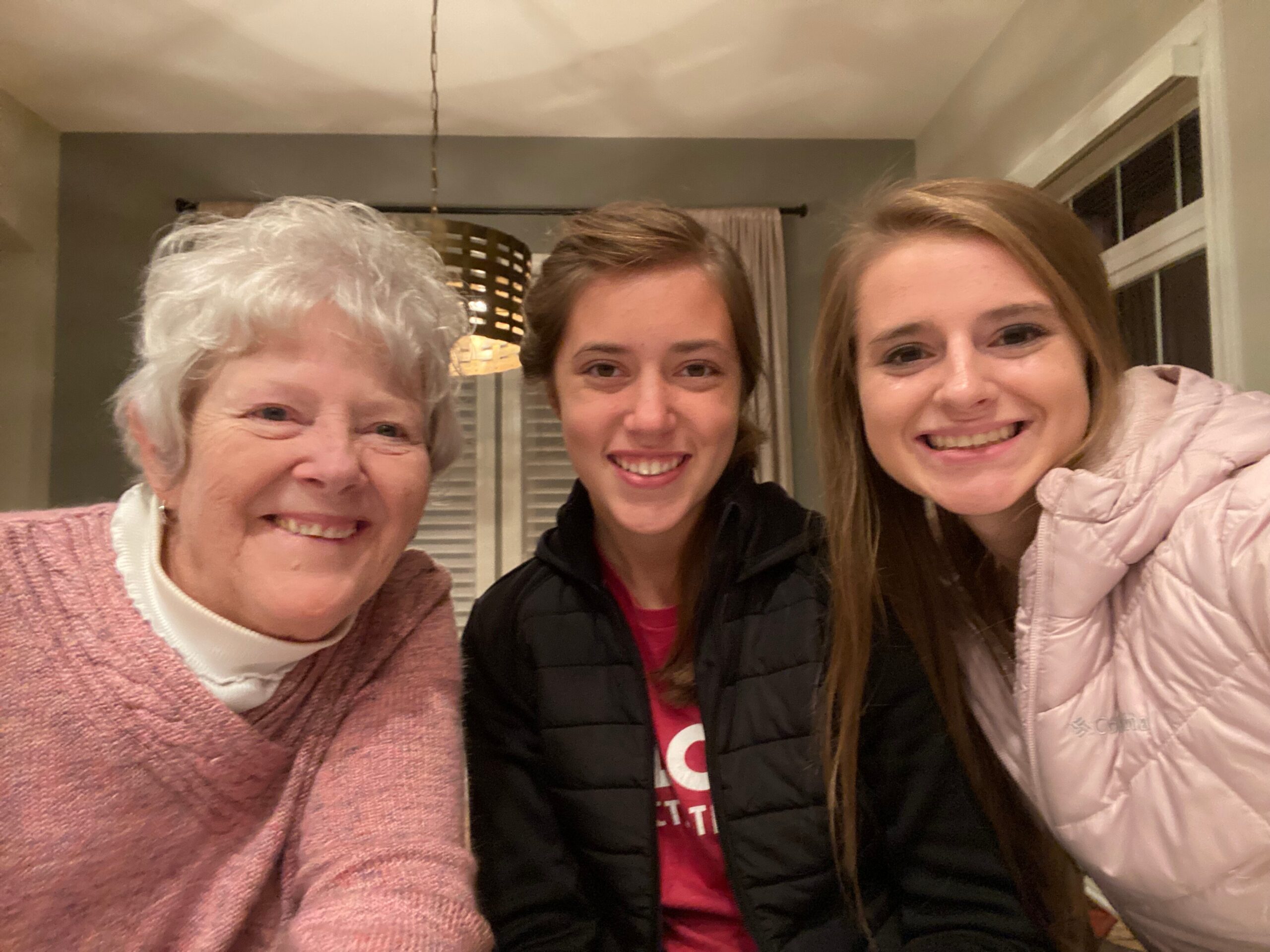 Three women smiling at the camera indoors, a close-up group selfie with warm lighting in the background.