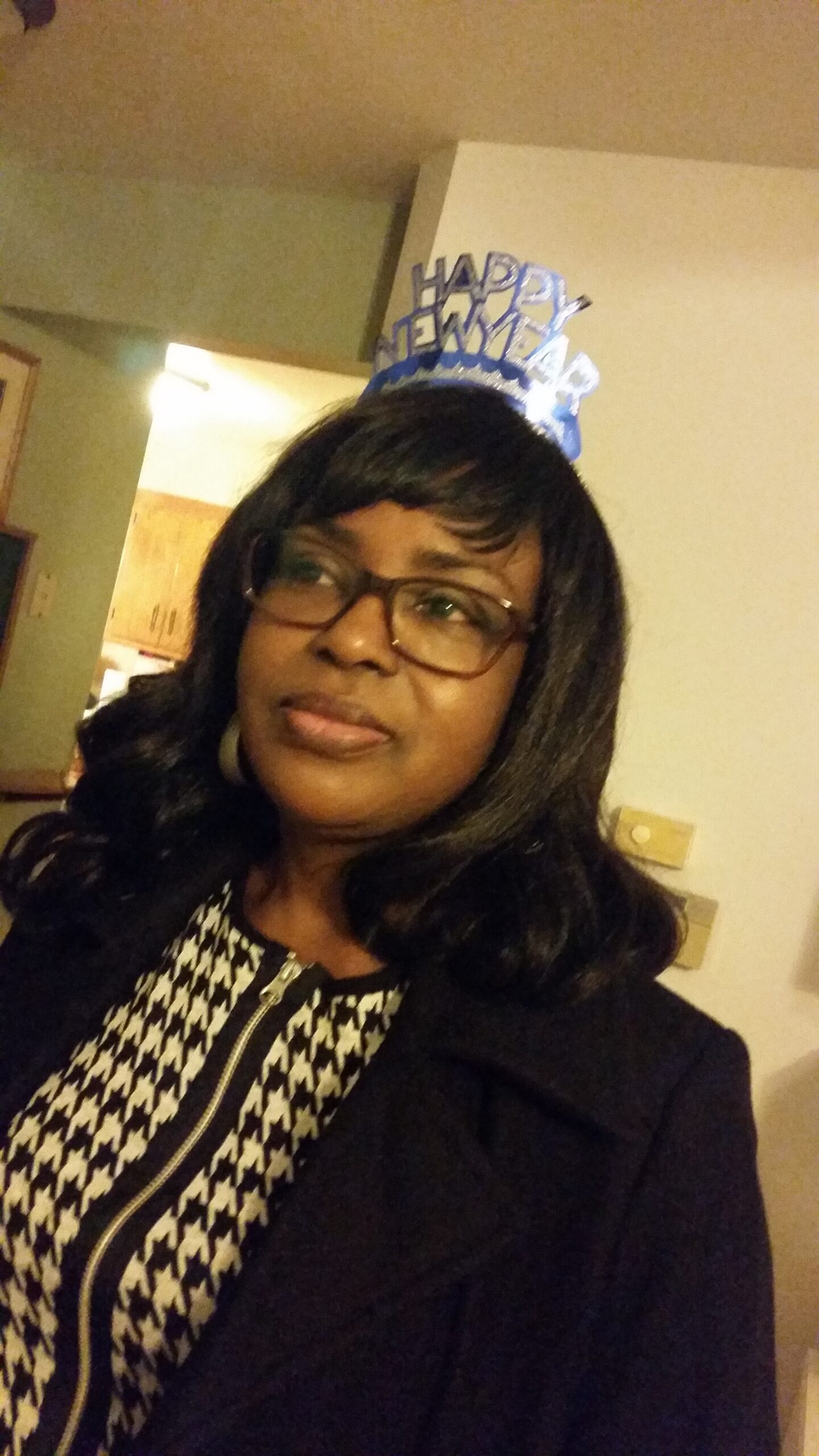 Woman with glasses wearing a blue 'Happy New Year' party hat, indoors.