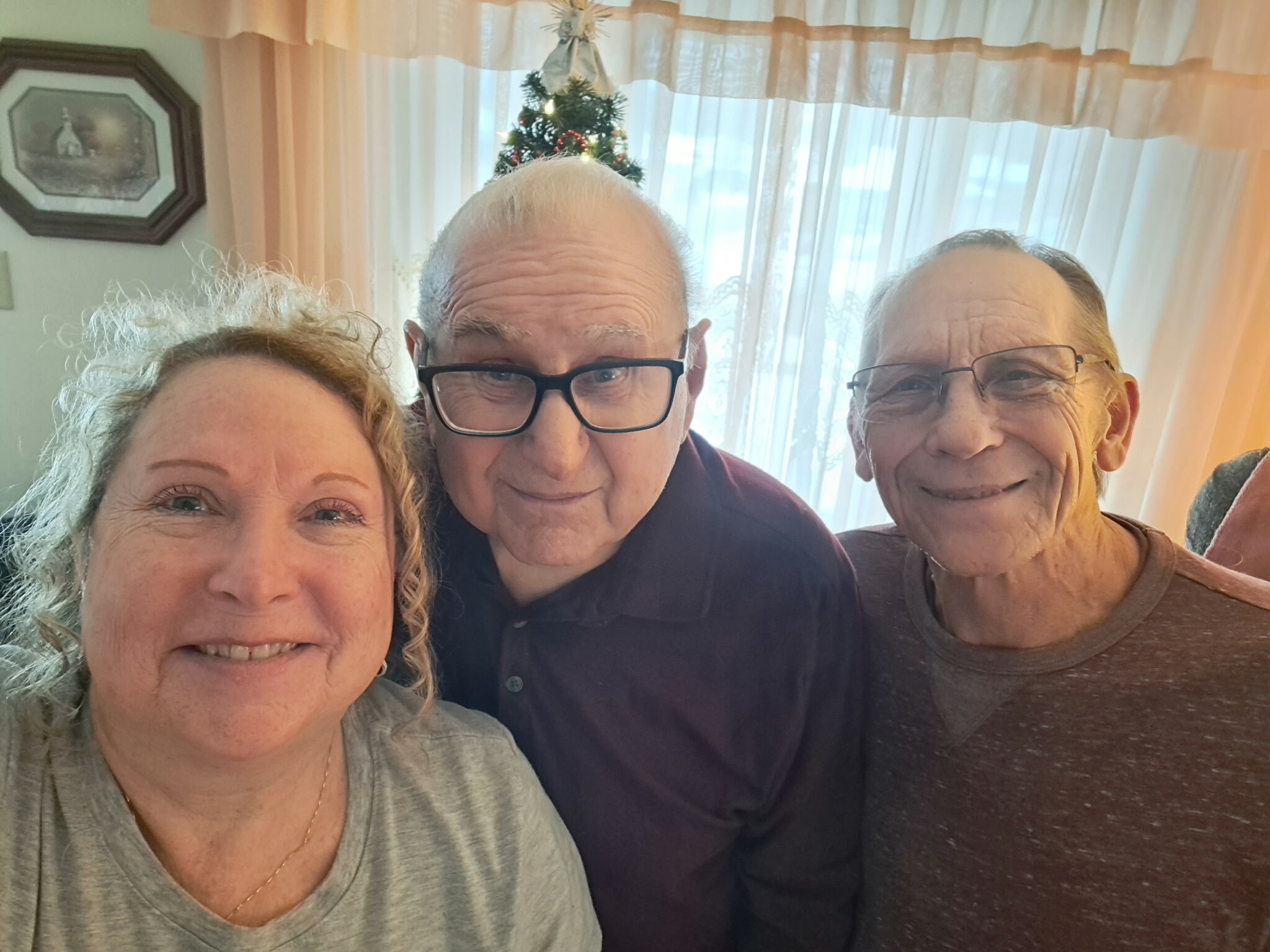Three seniors smiling in a close-up selfie indoors, with a small Christmas tree visible in the background.