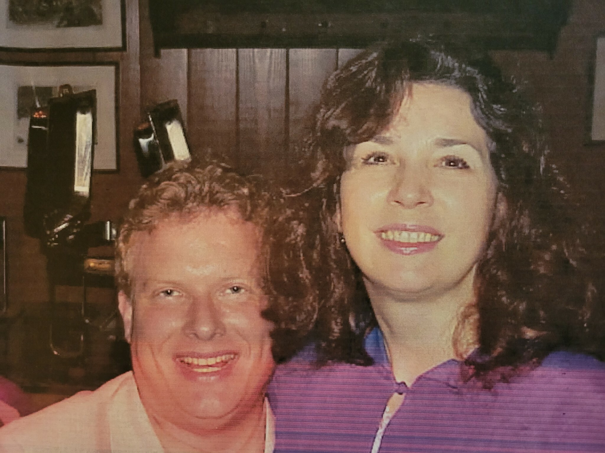 Two people smiling for a posed photo—a man in a white shirt in front with a woman beside him, both looking at the camera.