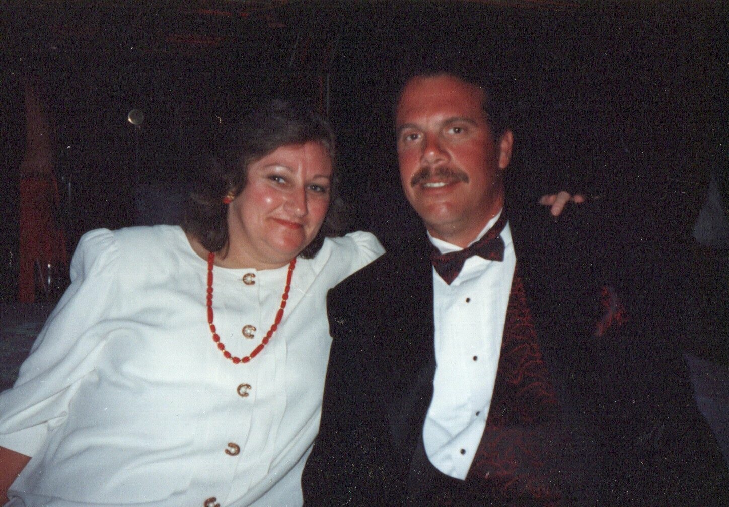 Smiling couple in formal attire posing together at a dimly lit event.